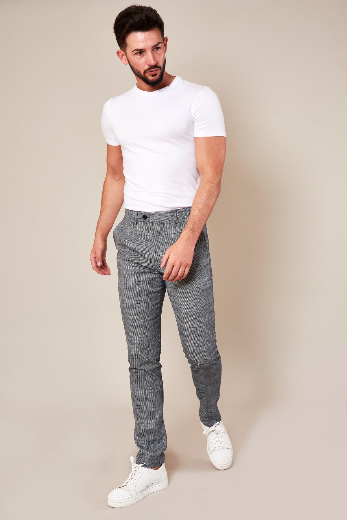 A bearded man with dark hair wears a white t-shirt and marcdarcy JERRY Skinny Fit Grey Check Trousers, standing against a beige background.