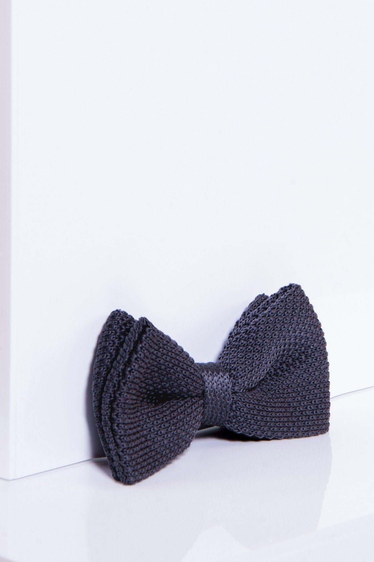 The marcdarcy KB - Knitted Double Layer Bow Tie in Mid Grey is pre-tied and rests against a white wall and surface, casting a soft shadow.