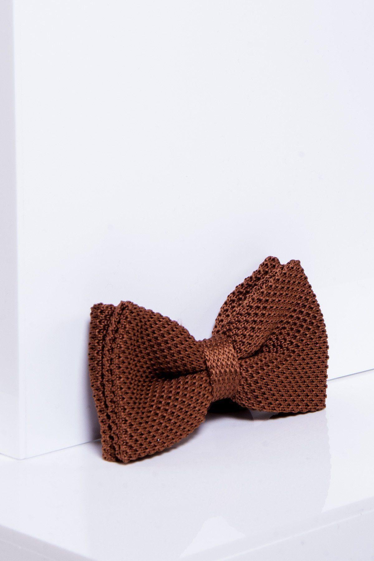 The marcdarcy KB - Knitted Double Layer Bow Tie In Rust, featuring a textured finish, is propped against a white wall and rests on a glossy white surface.