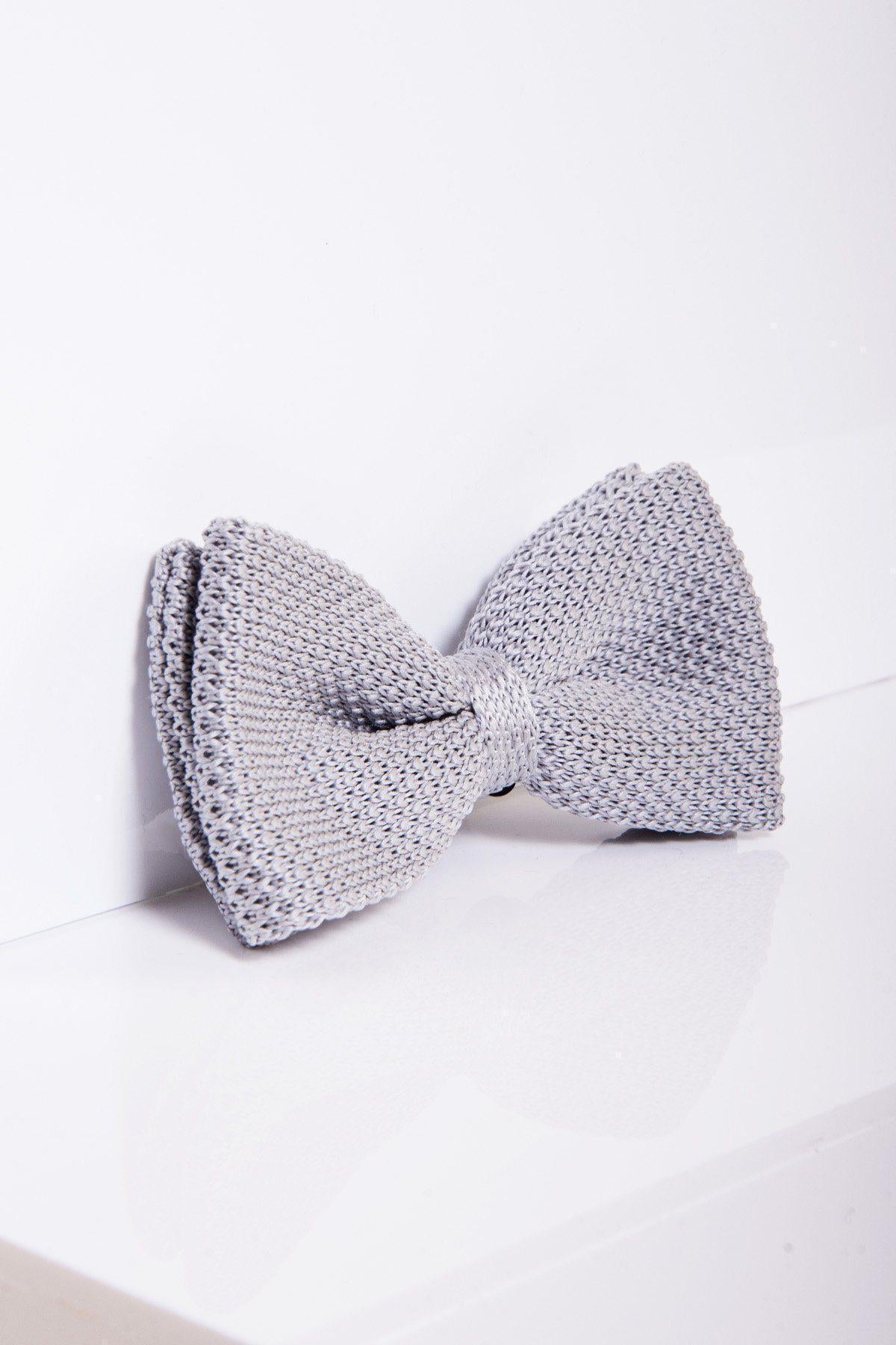 The marcdarcy KB - Knitted Double Layer Bow Tie in Silver Grey, from the spring/summer collection, is displayed on a glossy white surface, leaning against a white wall.