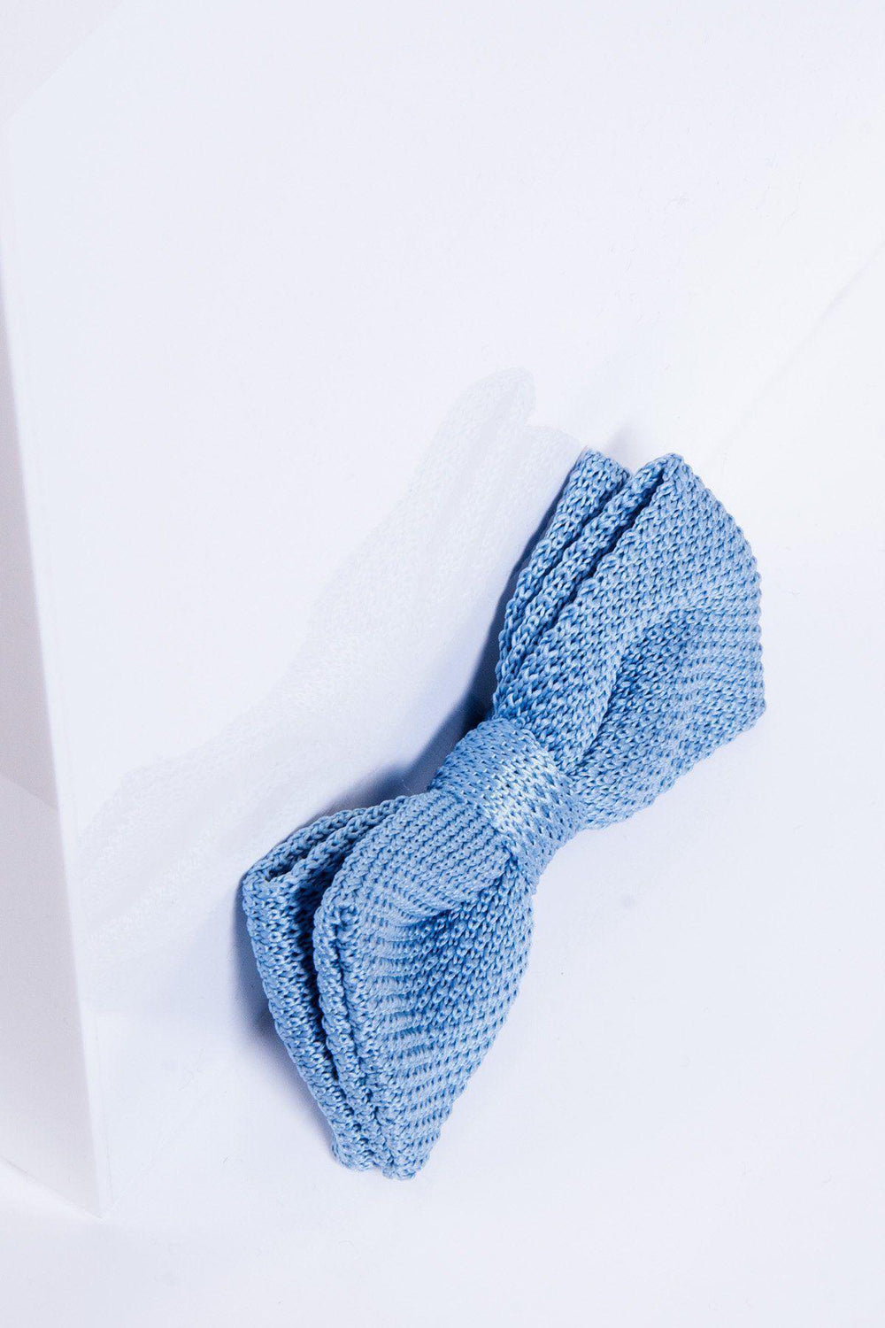 The marcdarcy KB - Knitted Double Layer Bow Tie In Sky Blue rests on a white surface with soft shadows and reflections, making it an ideal men's accessory for spring.