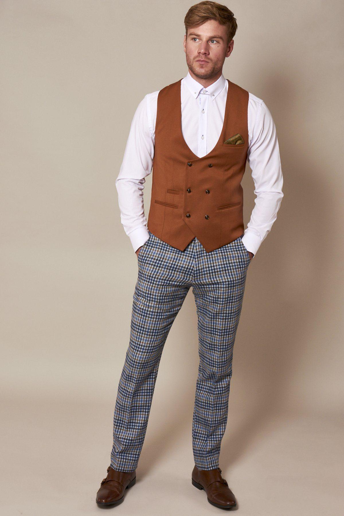 A man wears the marcdarcy KELLY Dark Tan Double Breasted Waistcoat with a white shirt and plaid pants, standing with his hands in his pockets.