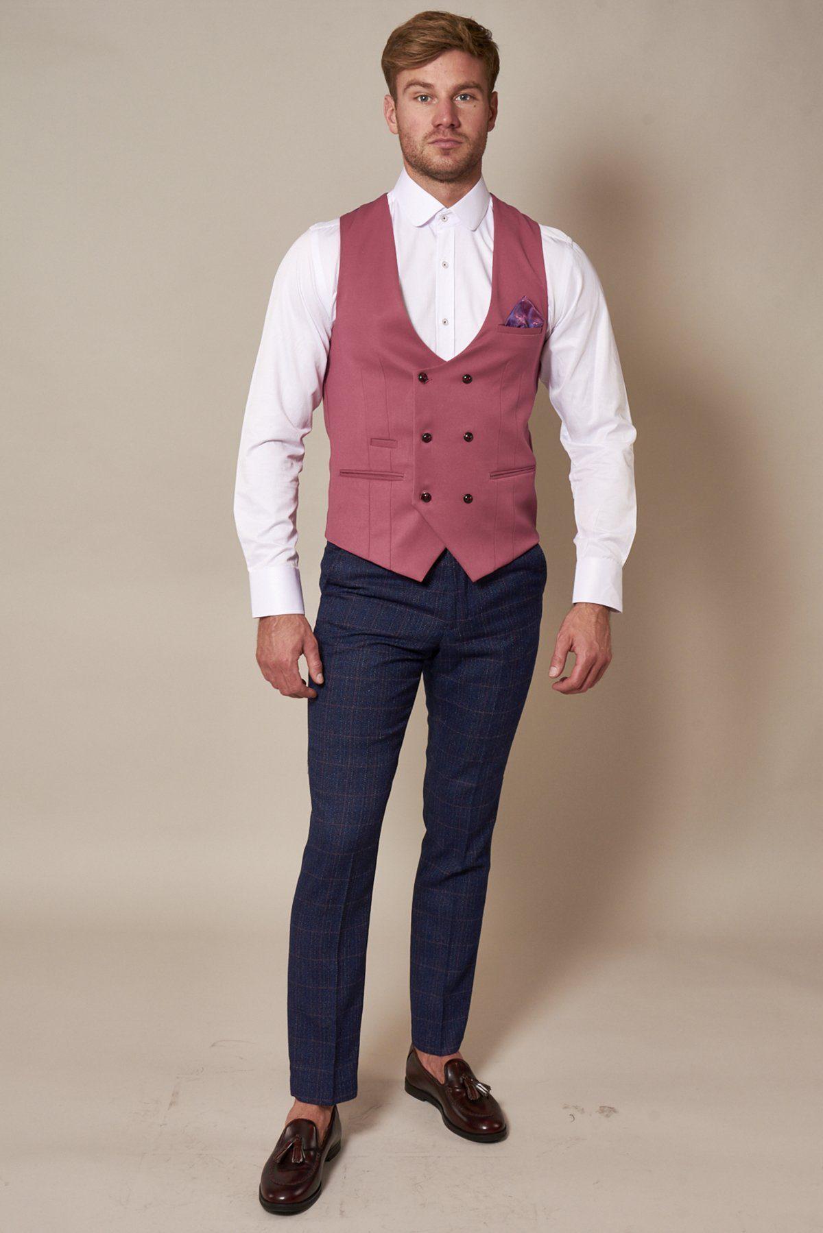 A man stands facing forward, wearing a marcdarcy KELLY pink double breasted waistcoat with purple paisley lining, a white dress shirt, dark blue plaid pants, brown loafers, and a pocket square. He has short hair and a trimmed beard.
