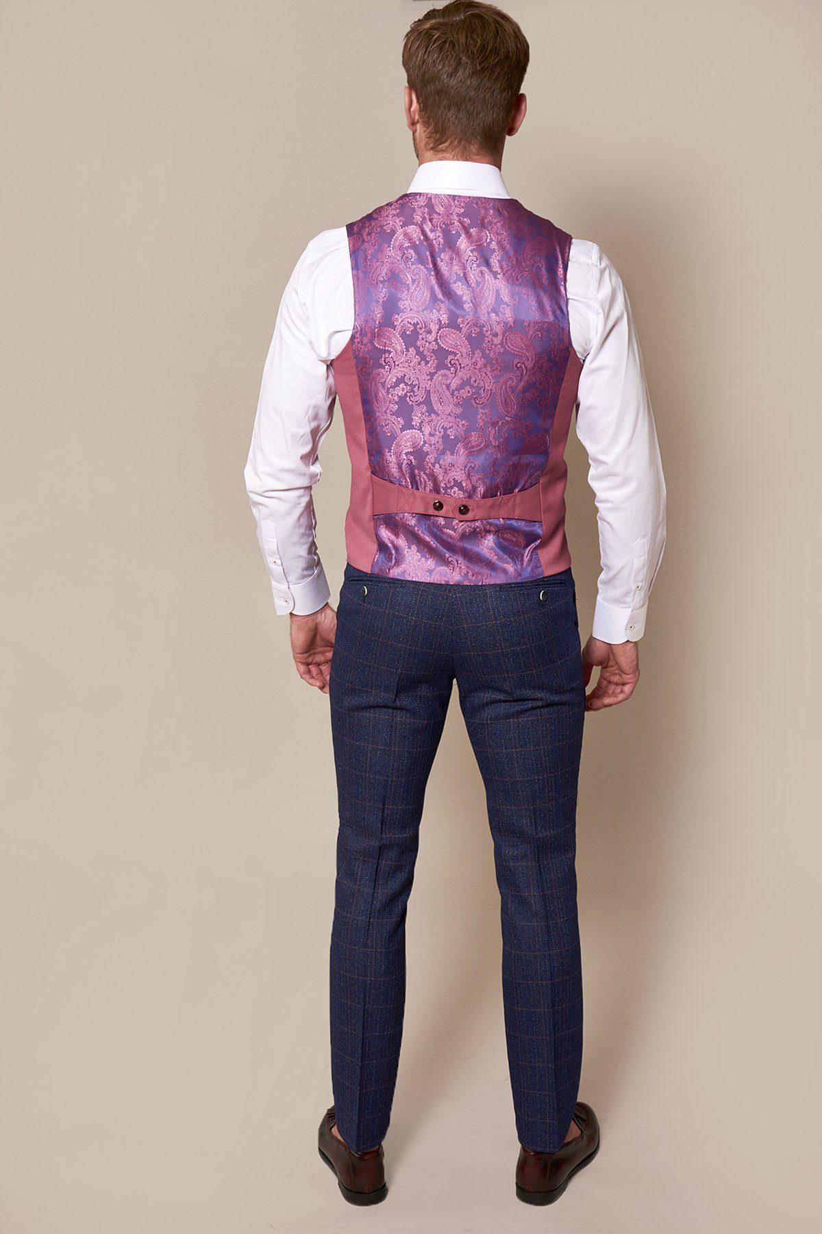 A man stands with his back to the camera in a white shirt, blue checked trousers, brown shoes, and a marcdarcy KELLY Pink Single Breasted Waistcoat featuring a silky finish, adjustable back strap, and purple paisley lining against a beige background.