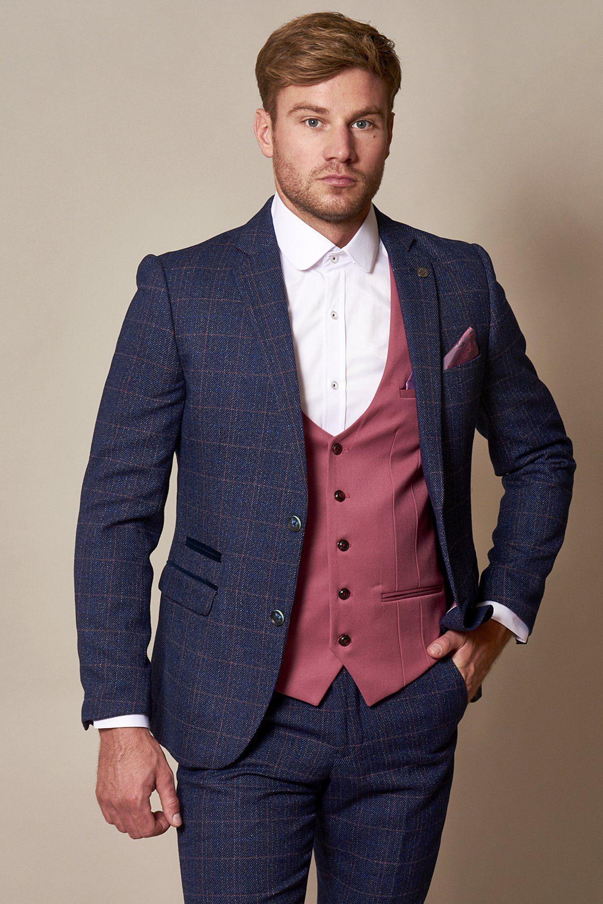 A man stands facing the camera, wearing a blue checked suit, white shirt, and the marcdarcy KELLY Pink Single Breasted Waistcoat. He has short brown hair, a trimmed beard, and his hand is in his pocket; the suit has a purple paisley lining.