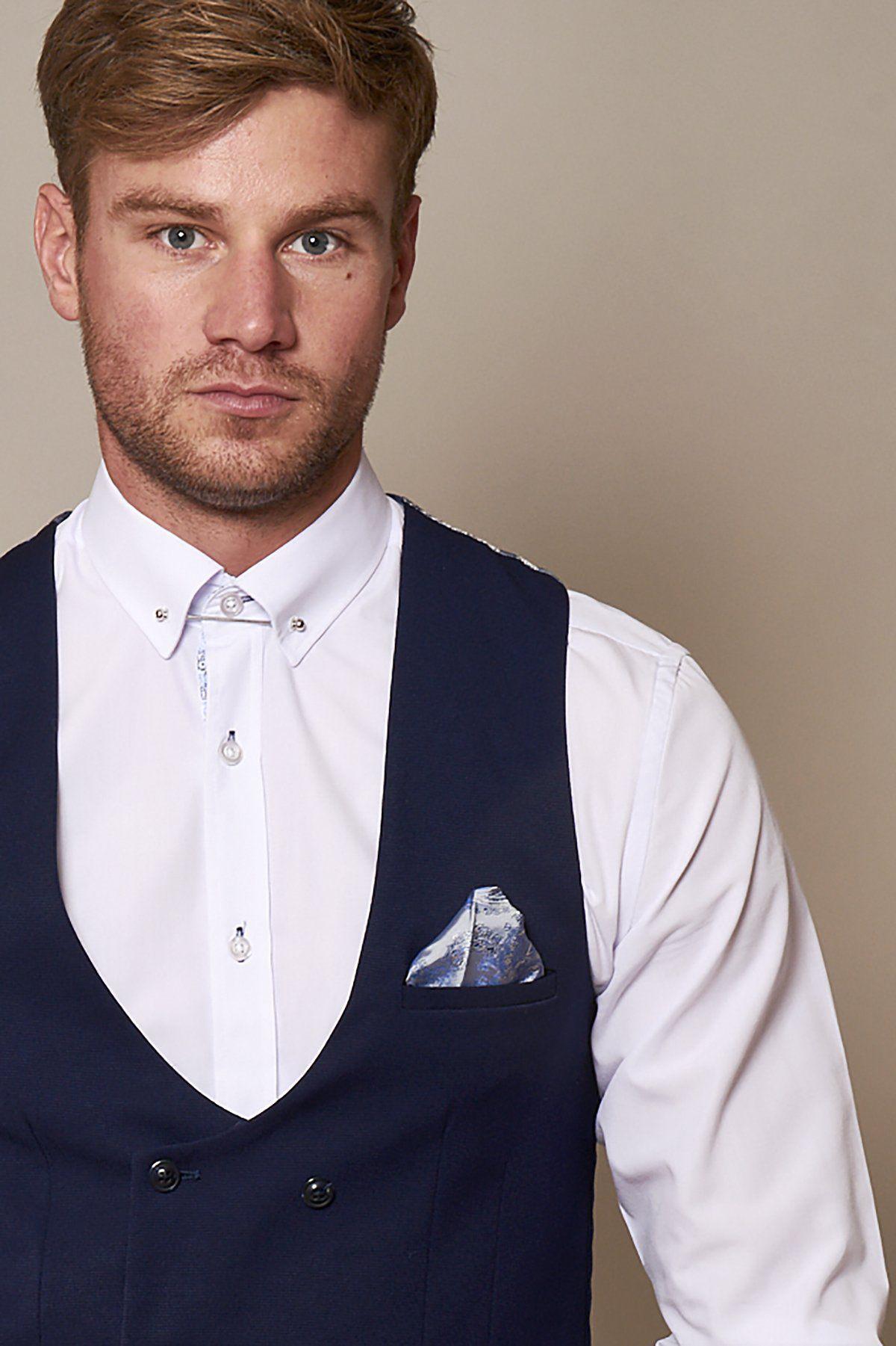 A man with light brown hair and a trimmed beard wears a white dress shirt and the marcdarcy KELLY Royal Blue Double Breasted Waistcoat with a blue patterned pocket square, standing against a plain beige background.