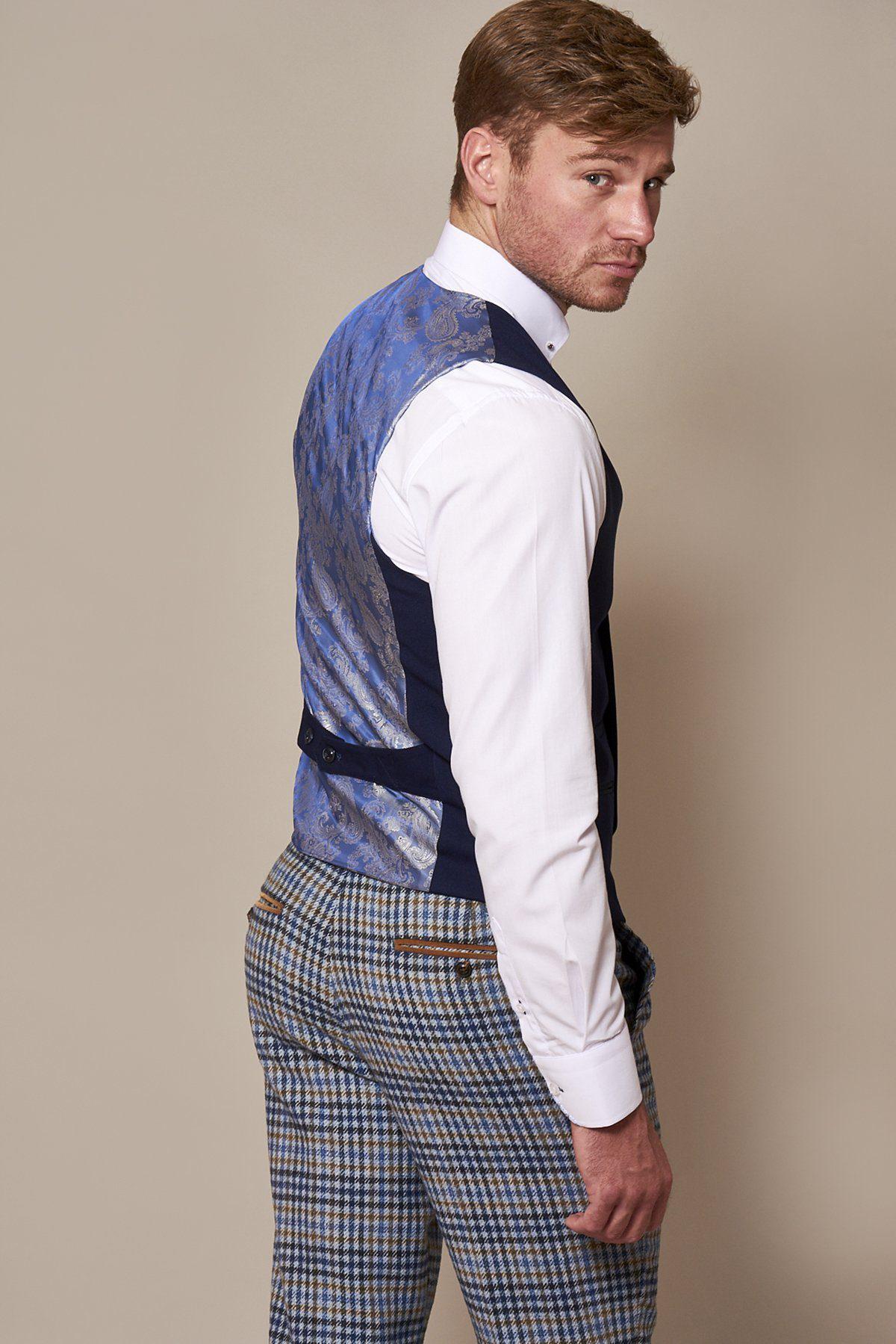 A man poses for a portrait wearing a white dress shirt, brown and blue plaid trousers, and the marcdarcy KELLY Royal Blue Double Breasted Waistcoat with paisley lining.