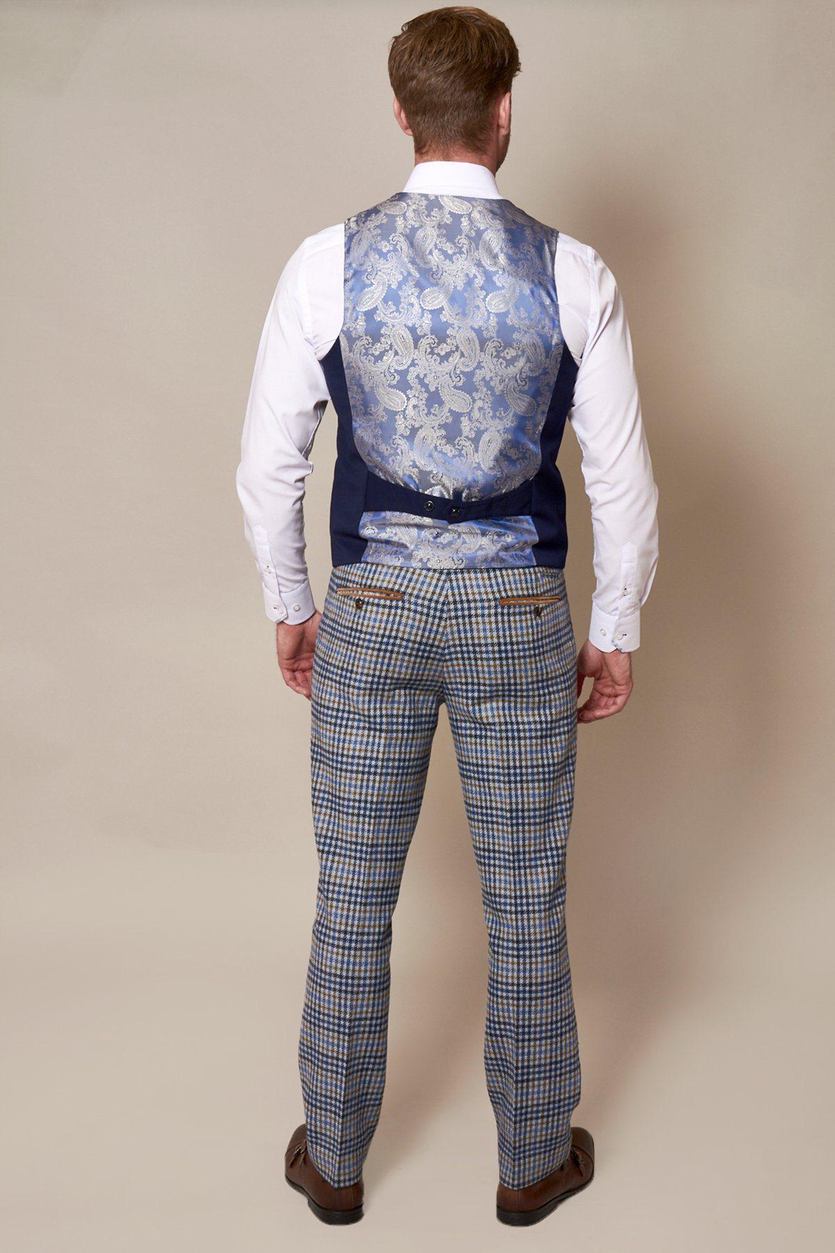 A man faces away in a crisp white shirt, marcdarcy's KELLY Royal Blue Double Breasted Waistcoat with a shiny floral back, light blue plaid trousers, and brown shoes against a plain light background.