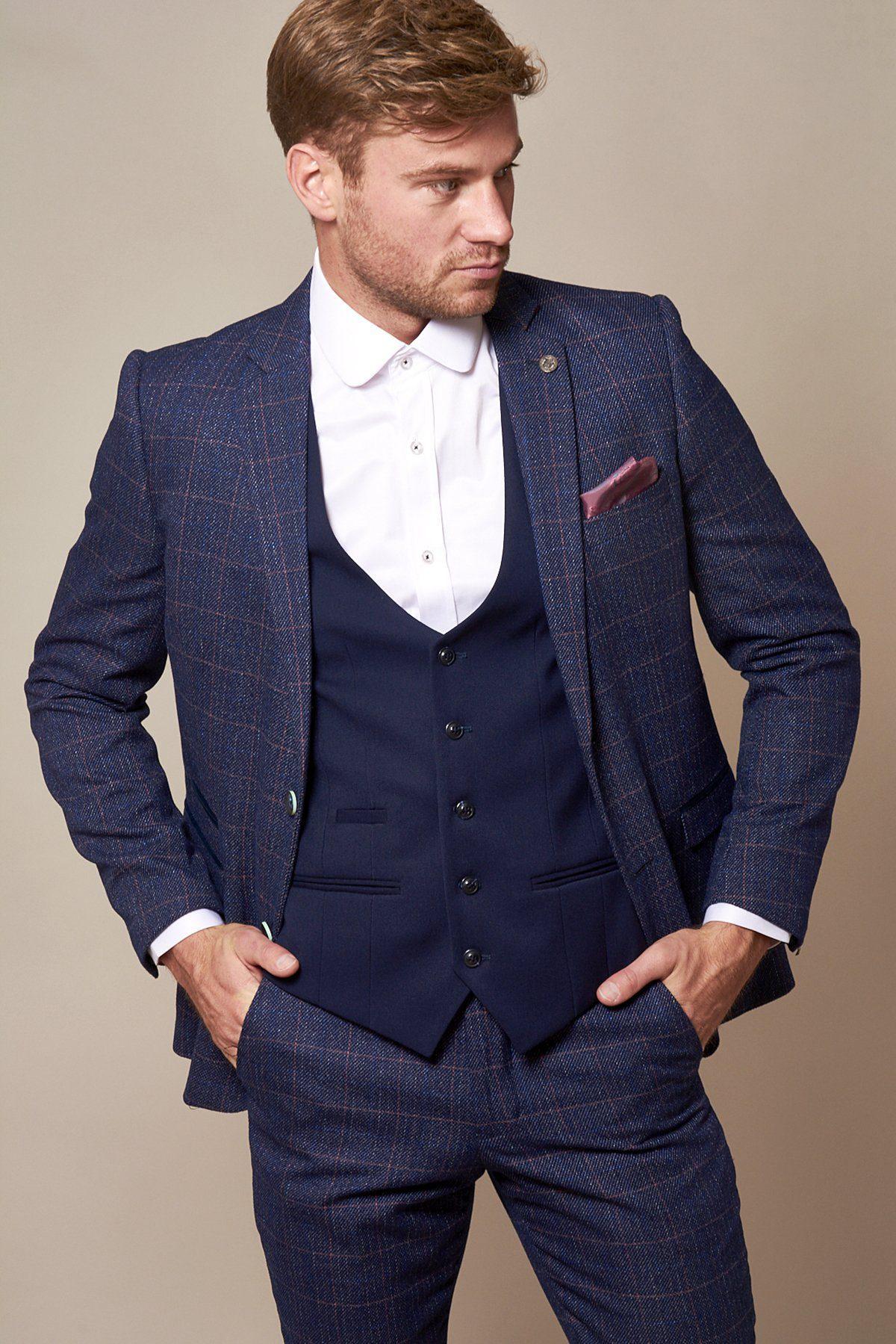 A man with short brown hair and a trimmed beard stands hands in pockets, wearing a marcdarcy KELLY Royal Blue Single Breasted Waistcoat over a white shirt, paired with a stylish blue plaid suit and navy vest, looking to the side.
