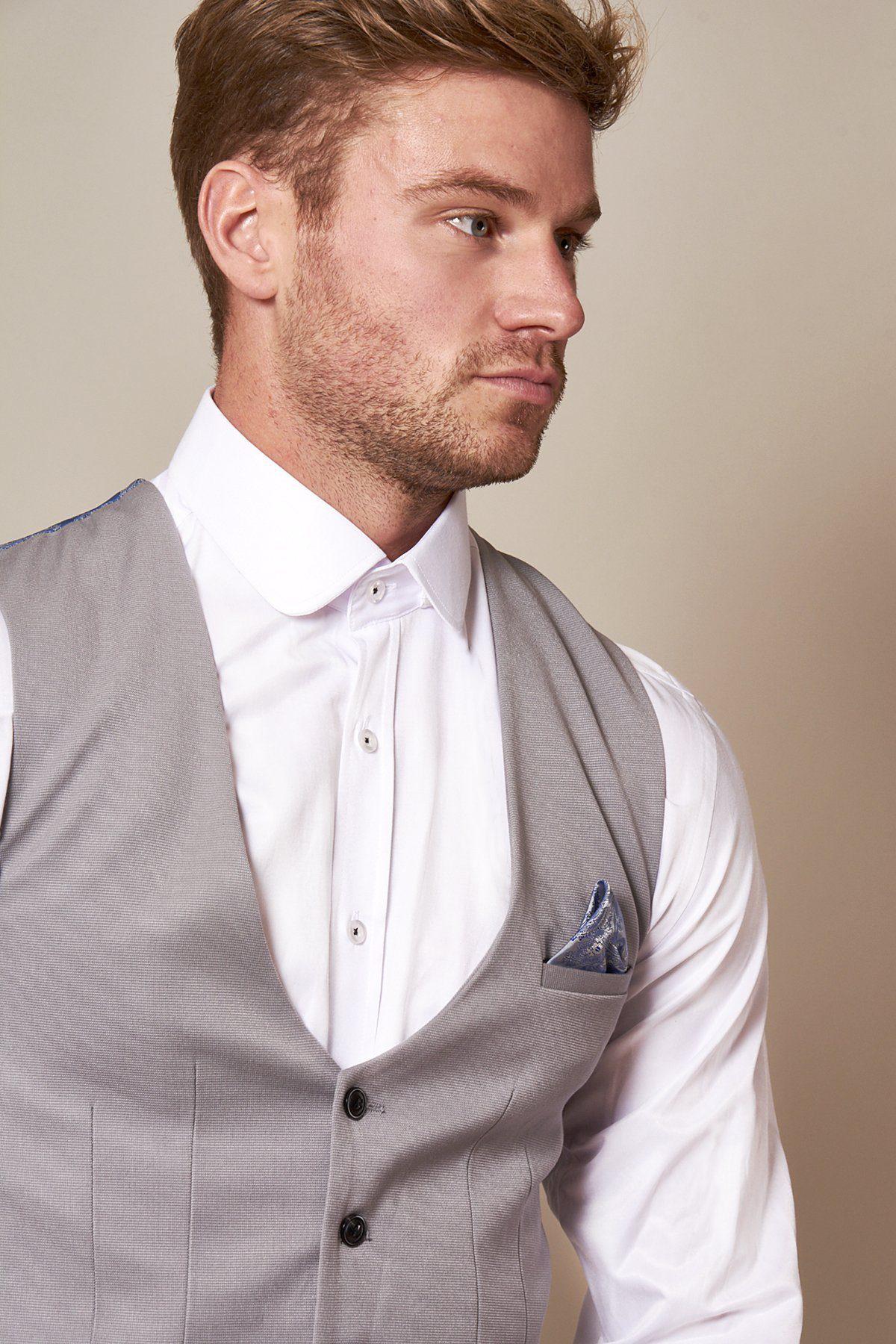 A man with light brown hair and a trimmed beard wears a slim fit white shirt and the marcdarcy KELLY Silver Grey Single Breasted Waistcoat with a blue pocket square, looking to the side against a neutral backdrop.