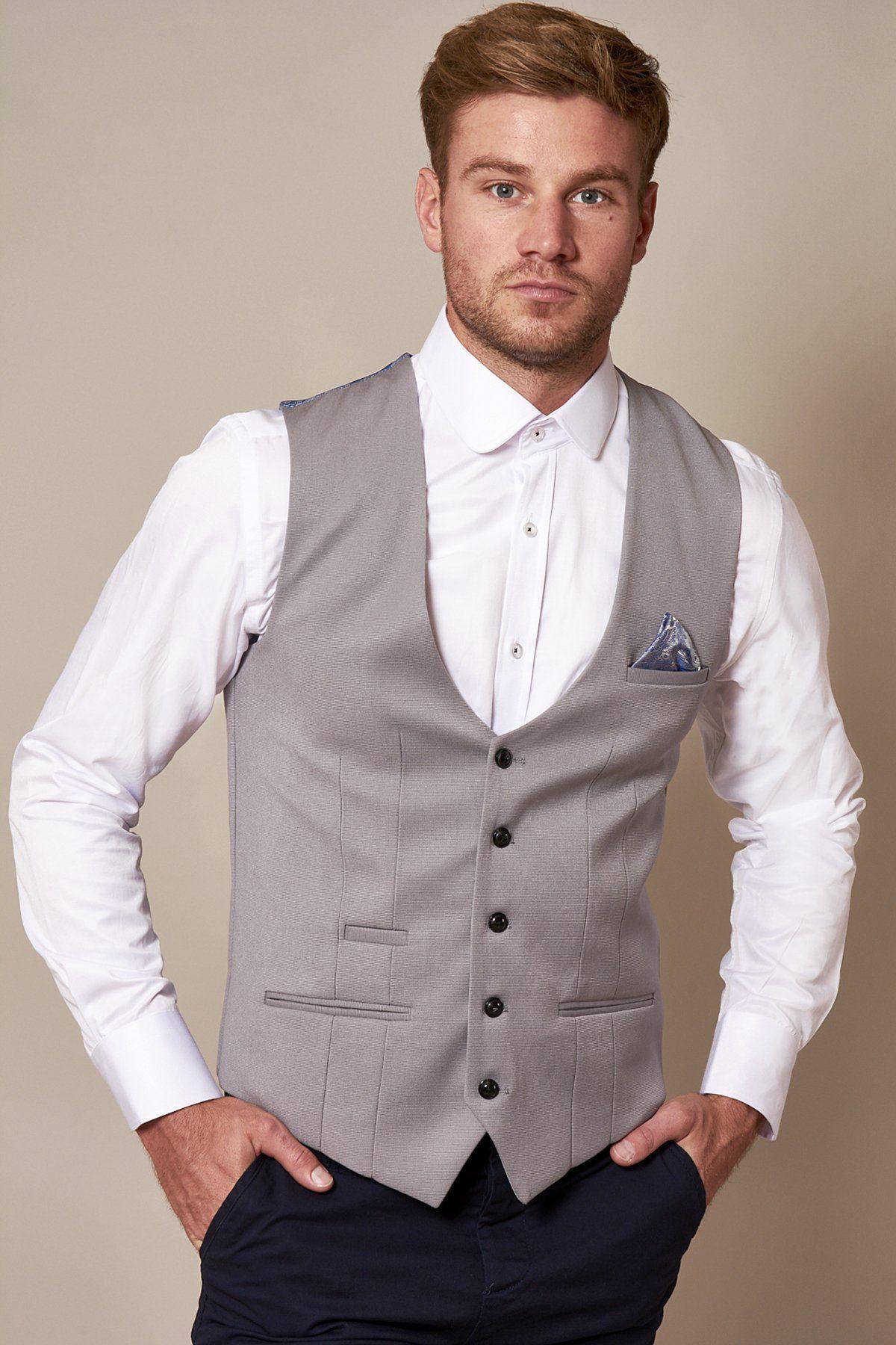 A man wears the marcdarcy KELLY Silver Grey Single Breasted Waistcoat over a white dress shirt with a pocket square and dark pants, standing with his hands in his pockets against a plain background.