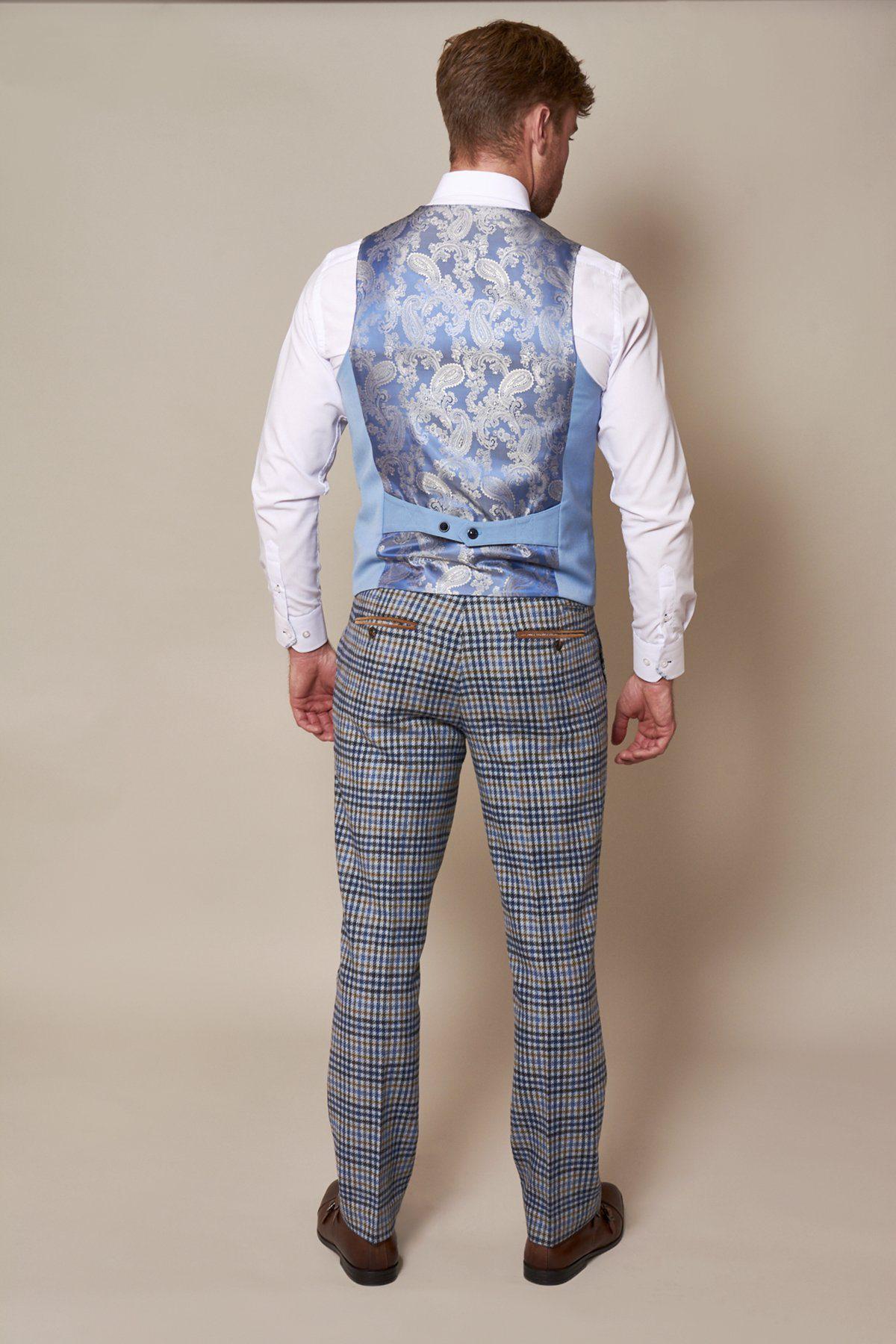 A man poses against a beige background, wearing the marcdarcy KELLY Sky Blue Double Breasted Waistcoat with a paisley back, paired with a white dress shirt, blue plaid trousers, and brown dress shoes.
