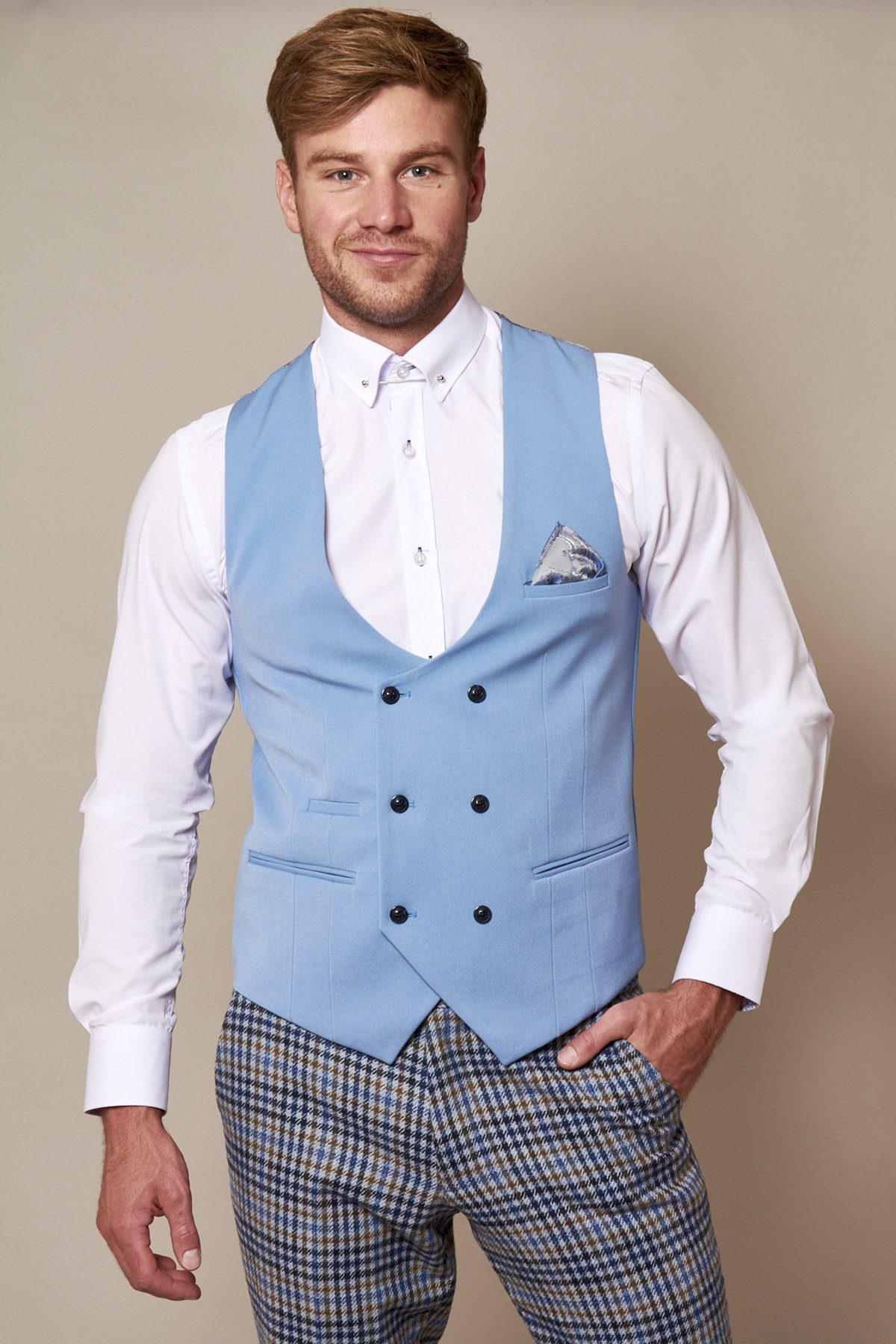 A man with short hair and a trimmed beard smiles slightly, wearing the marcdarcy KELLY sky blue double-breasted waistcoat over a white dress shirt, patterned check pants, and a pocket square against a plain background.
