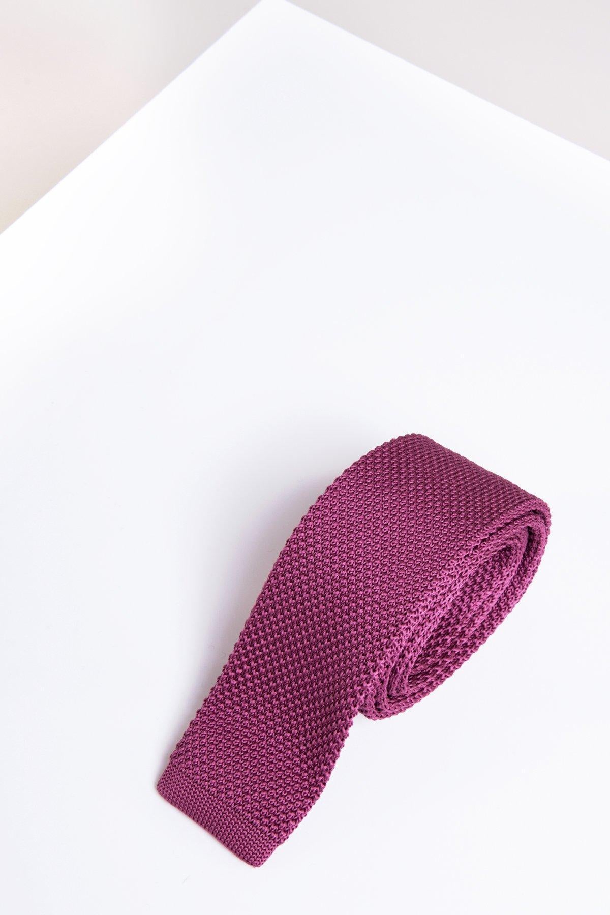 The KT - Berry Knitted Tie by Accessory, featuring textured detail, is rolled up and set on a minimalist white background—a modern men’s accessory.