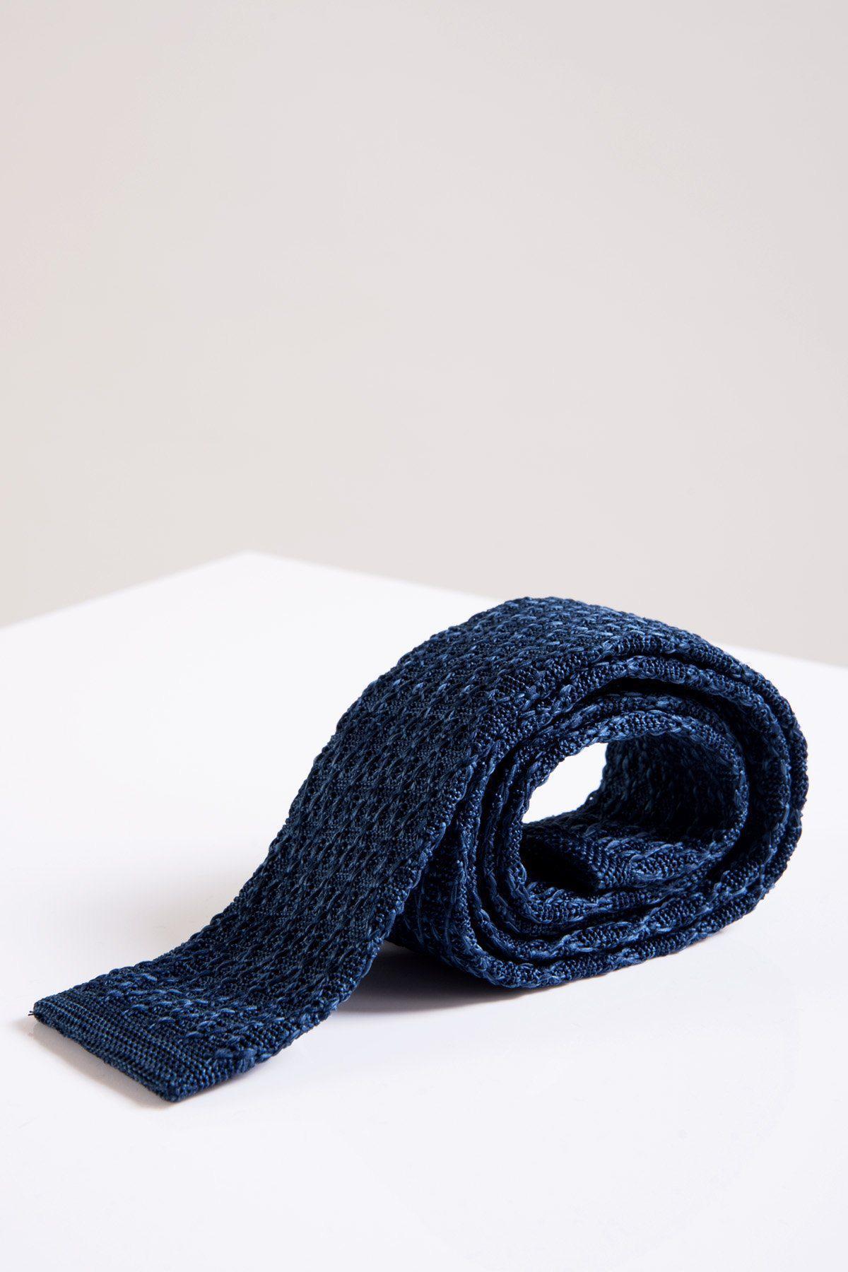 The Accessory KT - Blue Marl Knitted Tie, a versatile style essential, is rolled up and displayed on a white surface against a plain light background.