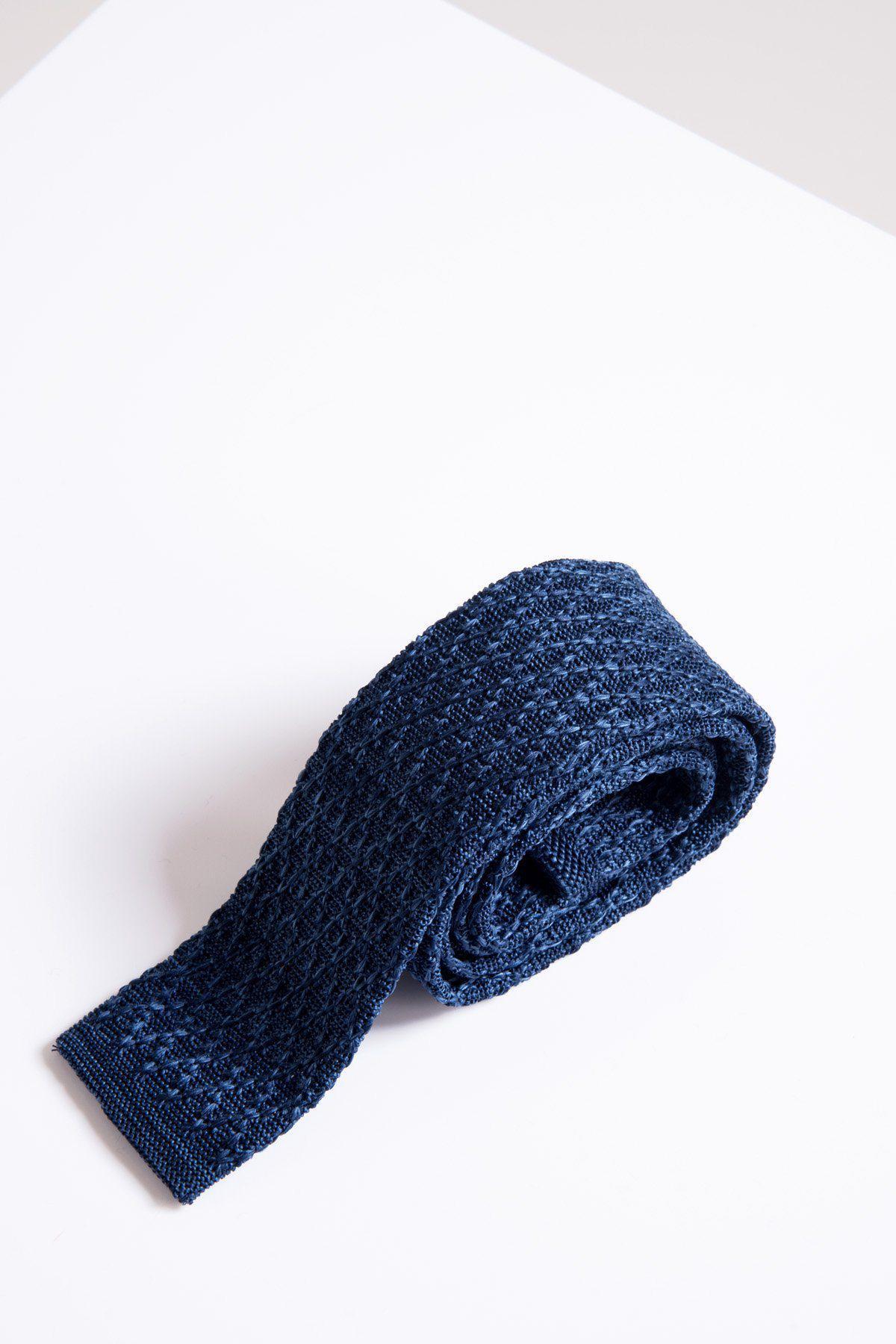The KT - Blue Marl Knitted Tie by Accessory is rolled up on a white surface with a minimal background, showcasing its textured blue marl knit for a versatile, casual style.