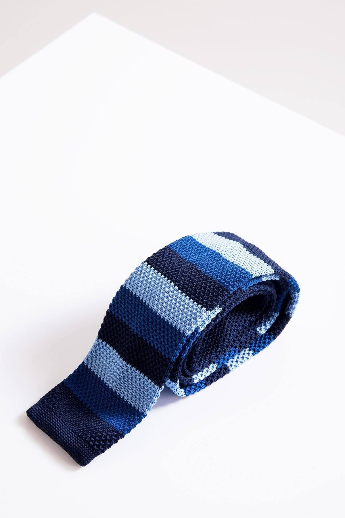 The Accessory KT - Blue Stripe Knitted Tie features horizontal blue stripes in a contemporary knit, rolled up and shown on a white surface—ideal for adding a casual touch to your office attire.