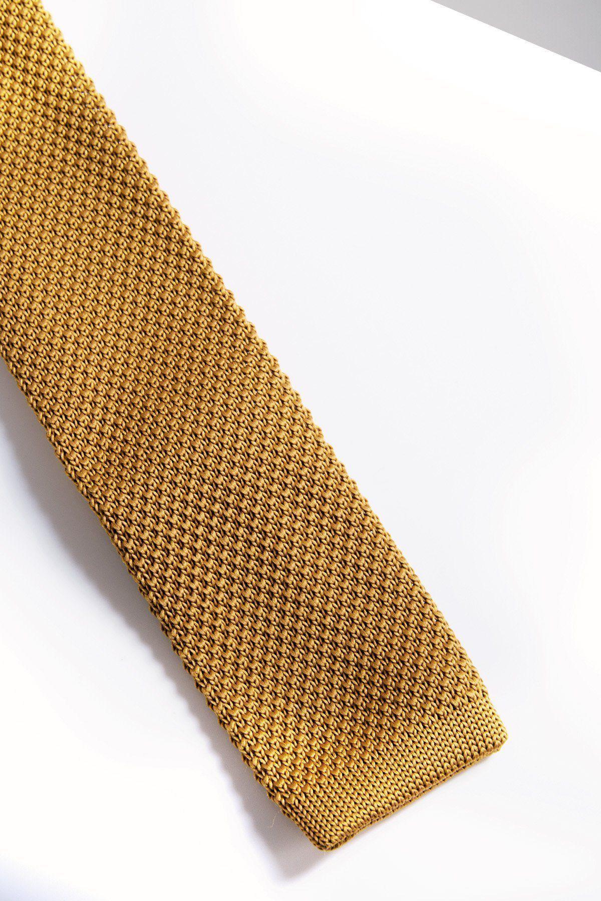 A close-up of the Accessory KT - Gold Knitted Tie on a white surface, highlighting its lightweight fabric and detailed modern knit design.