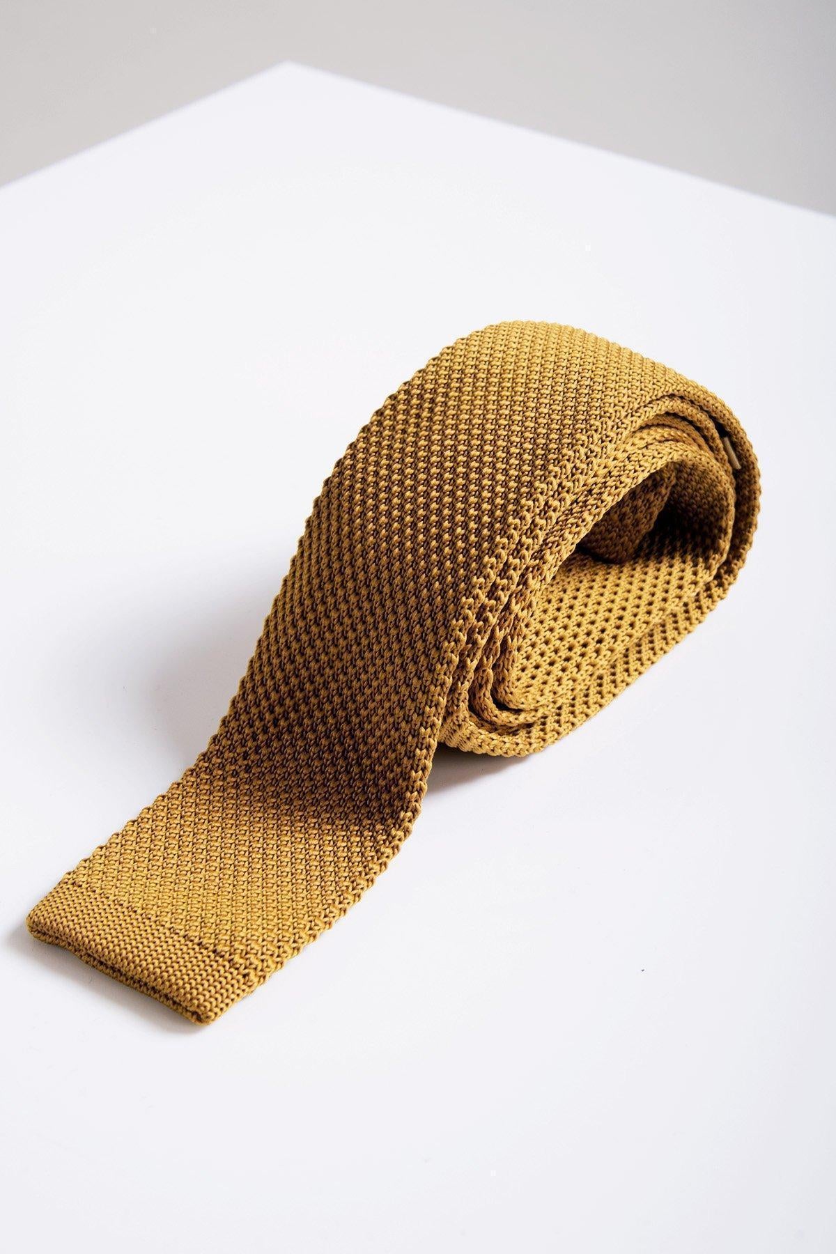The KT - Gold Knitted Tie by Accessory is neatly rolled on a white surface, highlighting its modern knitted design and textured details.