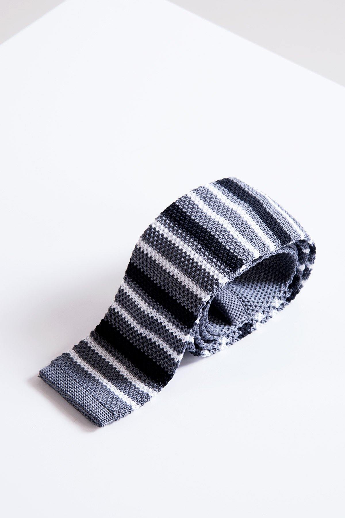 The Accessory KT - Grey Stripe Knitted Tie, neatly rolled, displays horizontal bands in grey, black, and white on a white surface.