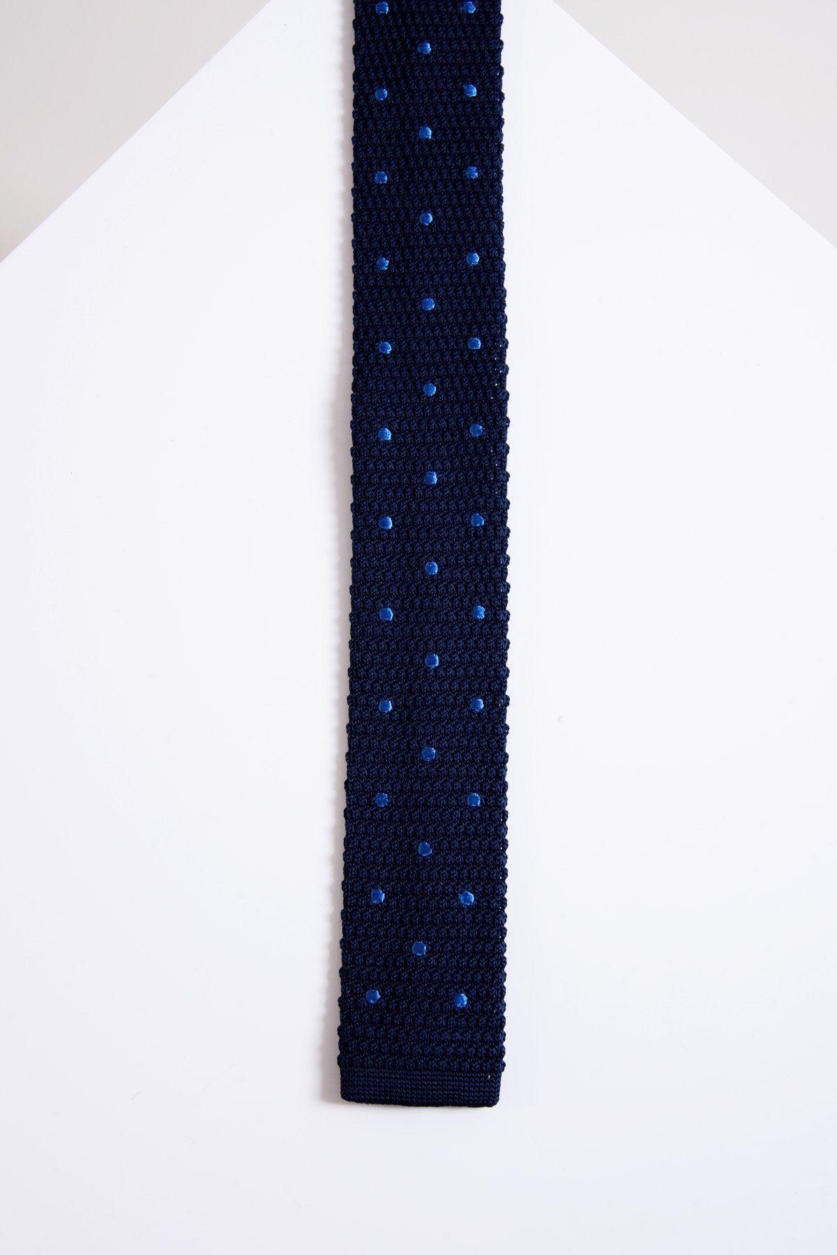 The Accessory KT - Navy Light Blue Spot Knitted Tie, featuring a modern navy knit with small blue spots, is displayed flat on a white surface with a geometric, house-shaped background.