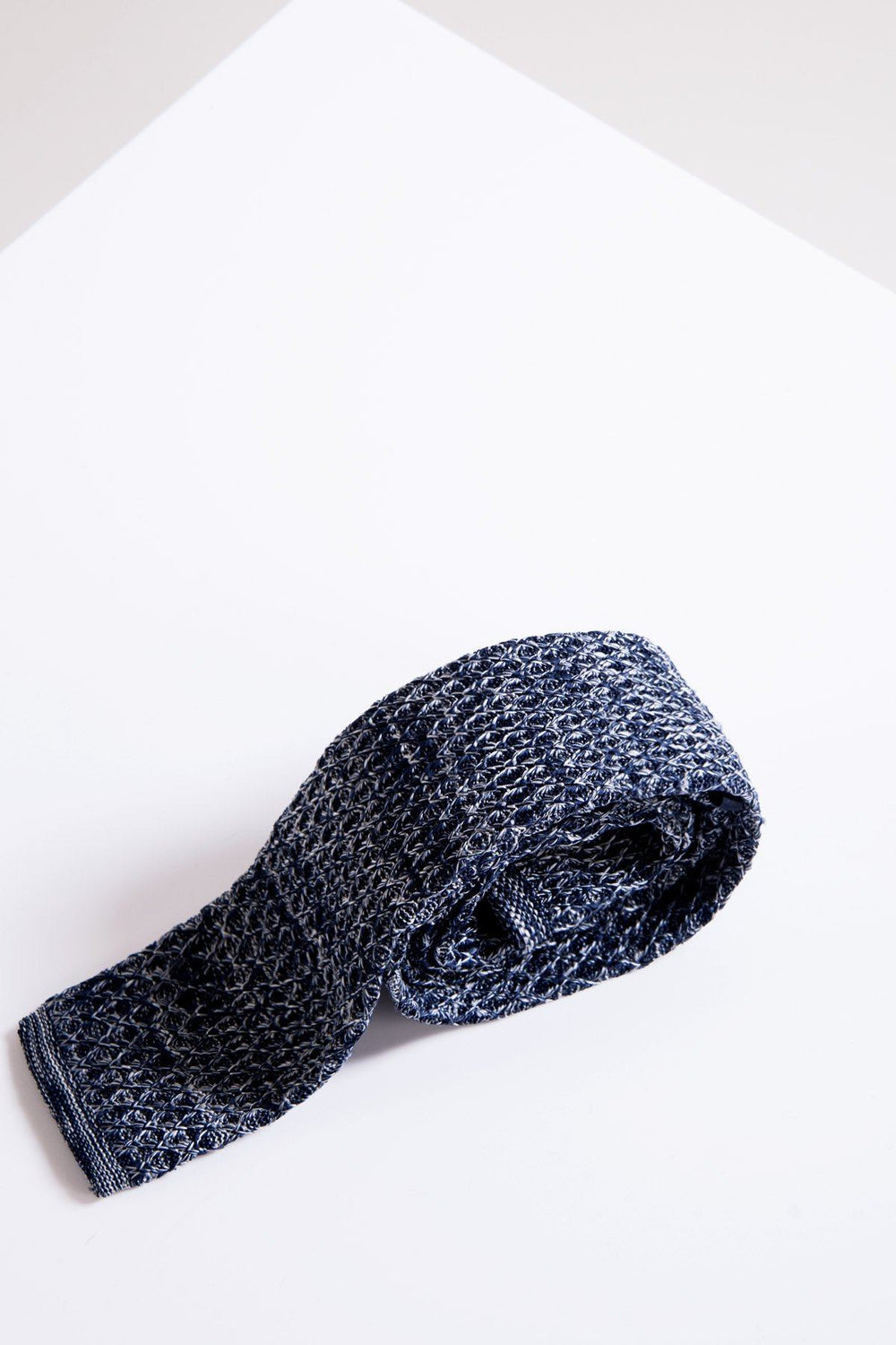 The Accessory KT - Navy Marl Knitted Tie features a white crisscross pattern and textured style, displayed rolled up on a white surface.