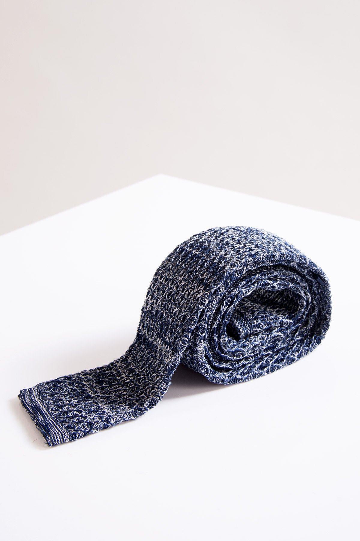 The Accessory KT - Navy Marl Knitted Tie, showcasing a modern textured knit, is rolled up and displayed on a white surface with a simple light backdrop.