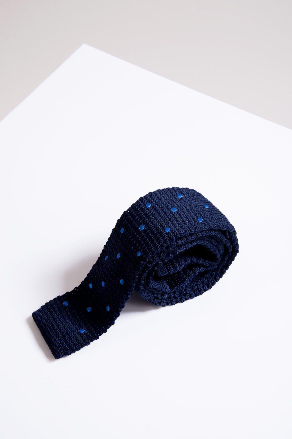 The Accessory KT - Navy Spot Knitted Tie, made from lightweight fabric and featuring small light blue polka dots, is neatly rolled and set on a white surface with angled edges.
