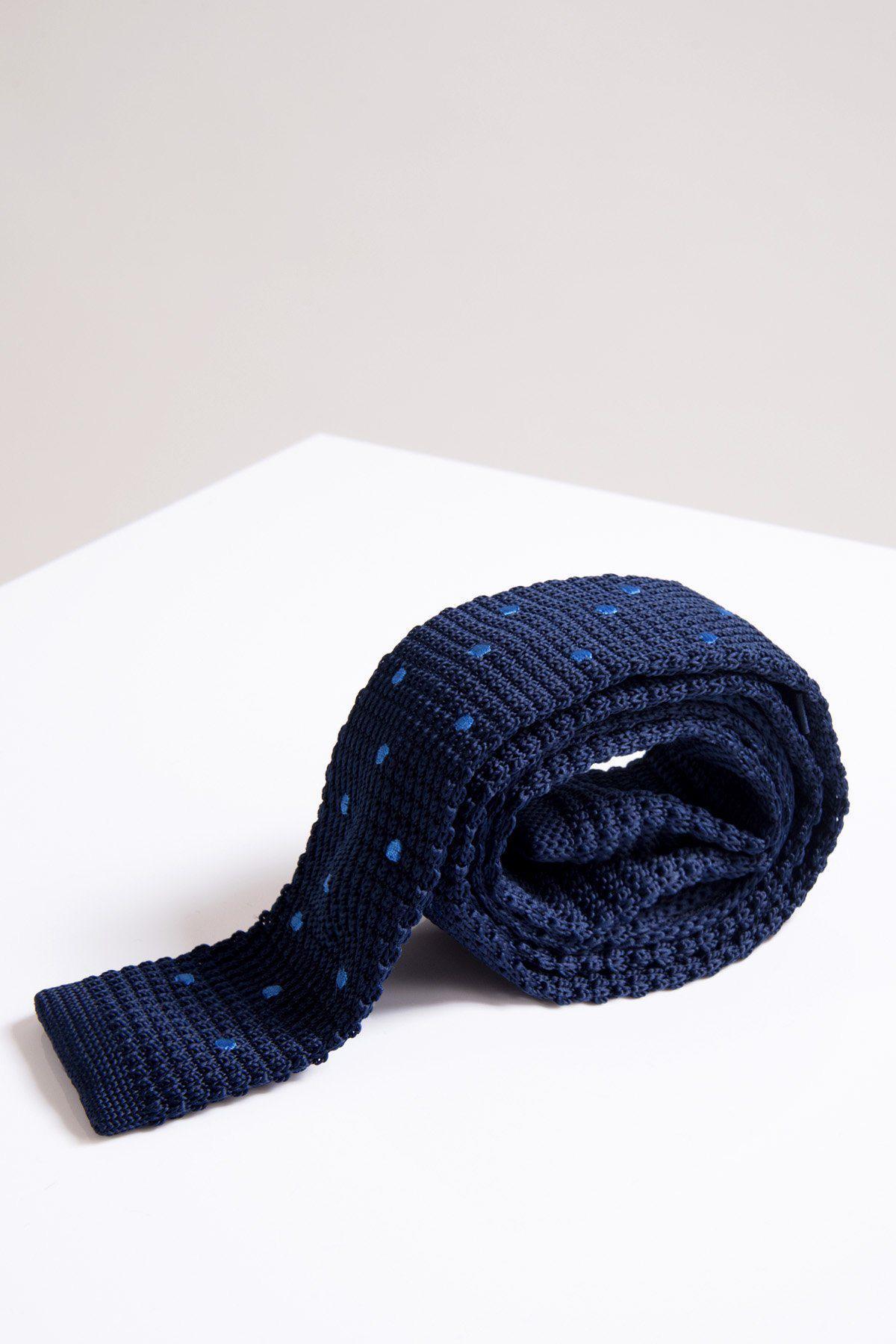 The Accessory KT - Navy Spot Knitted Tie, featuring a textured knit with light blue polka dots, is shown rolled up on a white surface against a light background.