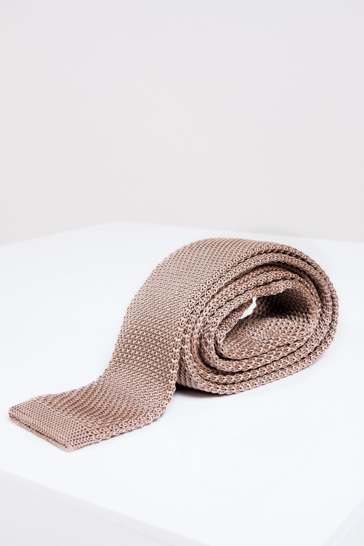 The Accessory KT - Oak Knitted Tie in beige oak, featuring a textured design, is rolled up on a white surface with a plain light background.