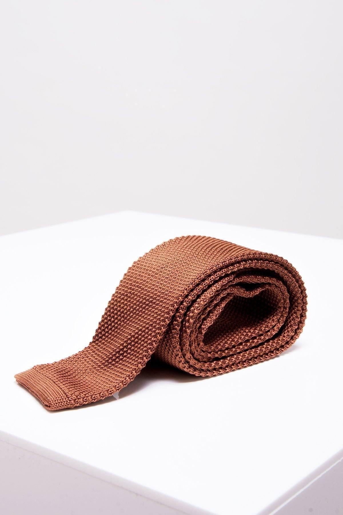 The KT - Rust Knitted Tie by Accessory, featuring a modern textured design in brown rust, is shown rolled up on a white surface against a plain light background.