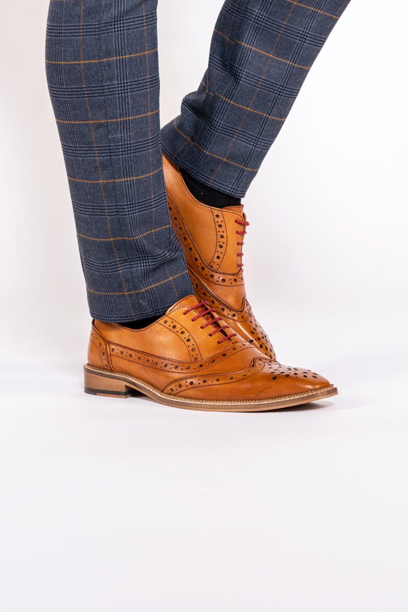A person wearing blue plaid pants and Marc Darcys LARKIN Mid Tan Leather Brogue Shoes with red laces stands against a white background.