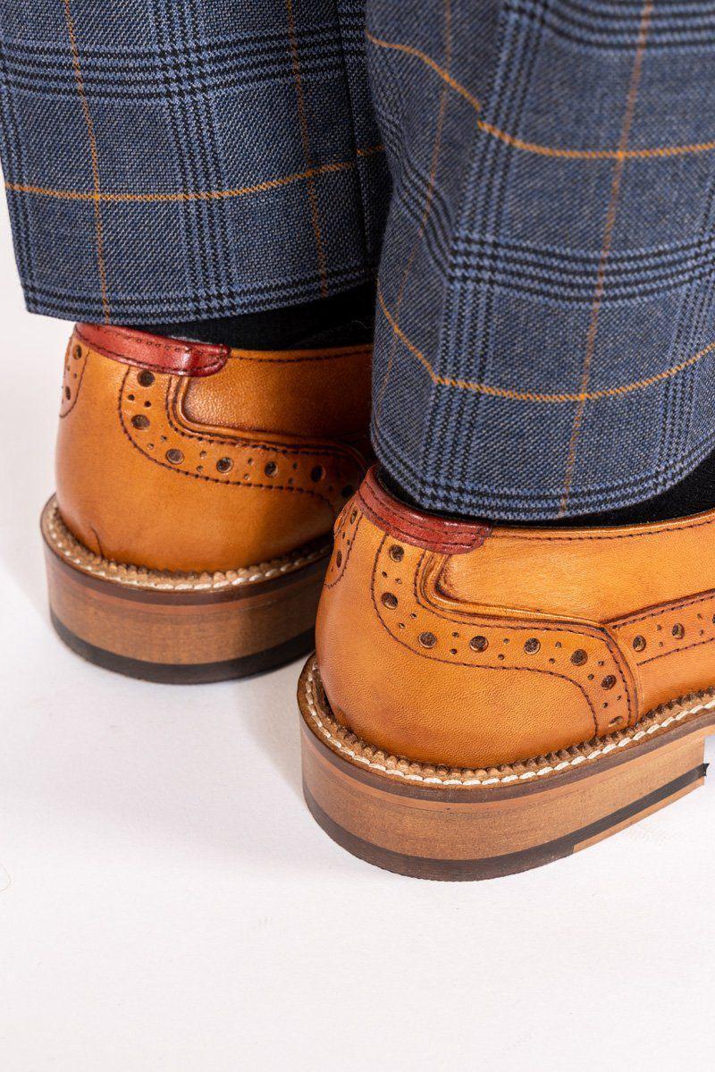 Close-up of a person wearing Marc Darcy LARKIN Mid Tan Leather Brogue Shoes with detailed hand-stitching, paired with blue plaid trousers. The image focuses on the back of the shoes and the lower part of the trousers.