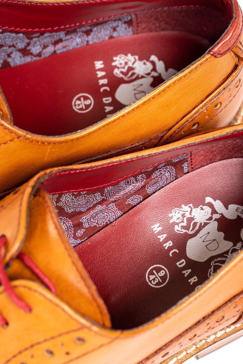 Close-up of two mid tan full grain leather LARKIN brogue shoes by Marc Darcy, featuring red laces, red insoles with white paisley lining, and the MARC DARCY logo with MD initials.