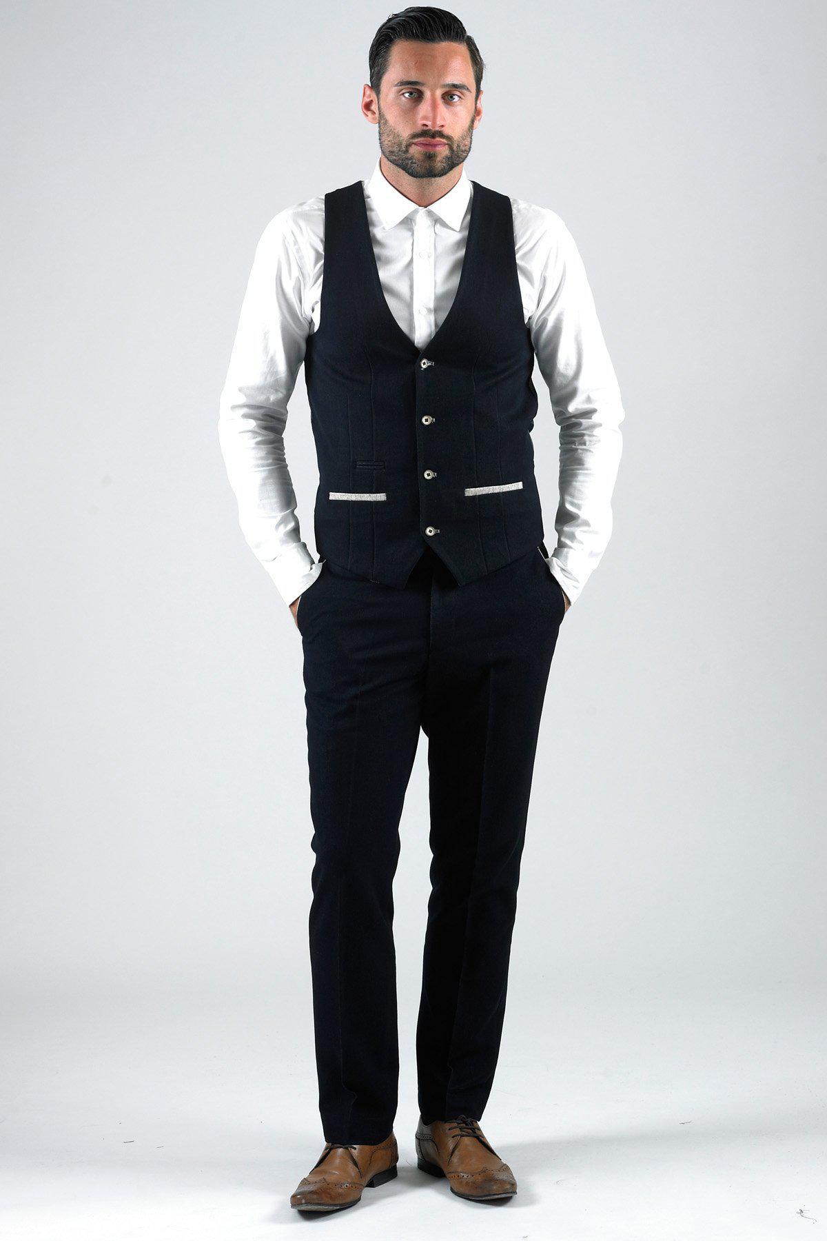 A man poses with his hands in his pockets wearing a marcdarcy LEE WILL Denim Look Navy Waistcoat, white dress shirt, black pants, and brown dress shoes.
