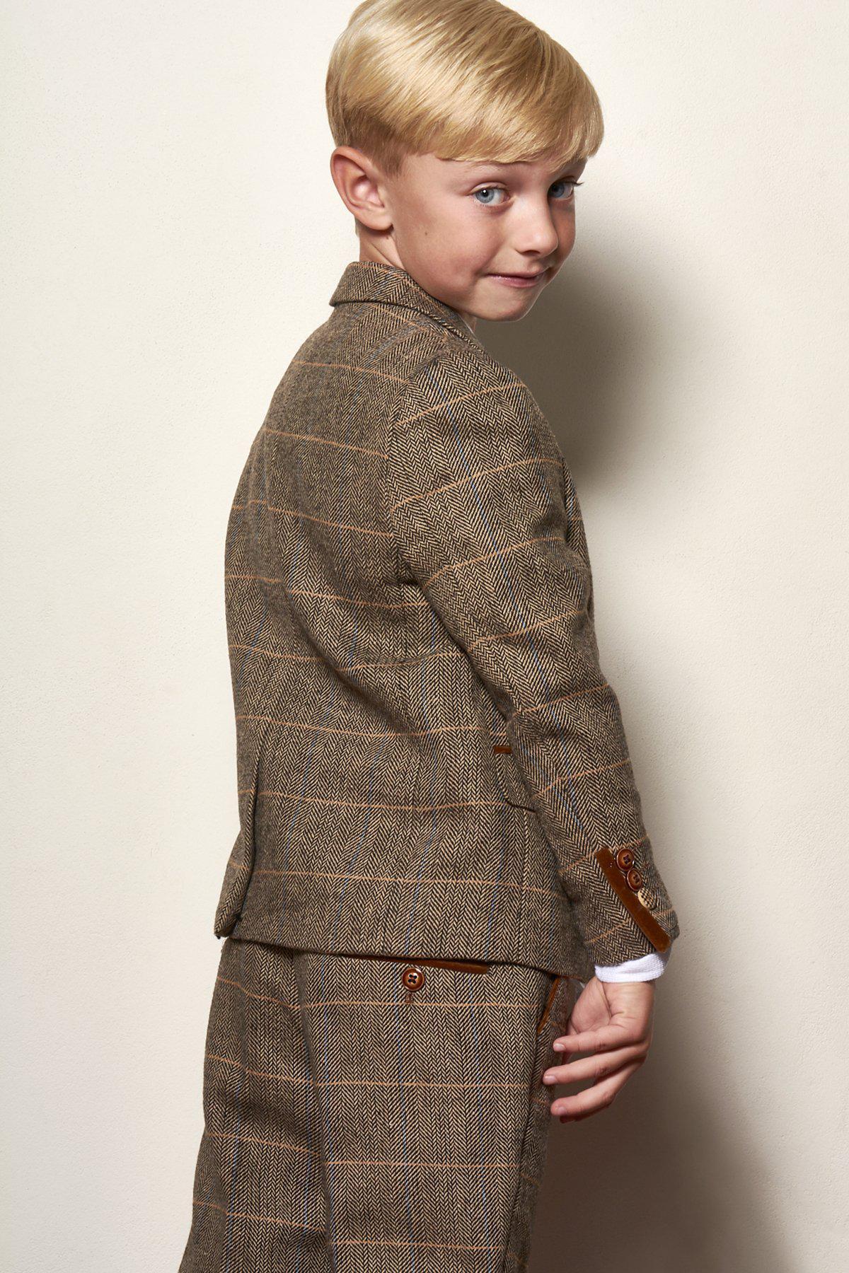A young boy smiles over his shoulder, dressed in the marcdarcy Matching Father & Son | Men’s TED Tan Tweed Check Three Piece Suit—ideal for a stylish country barn wedding.