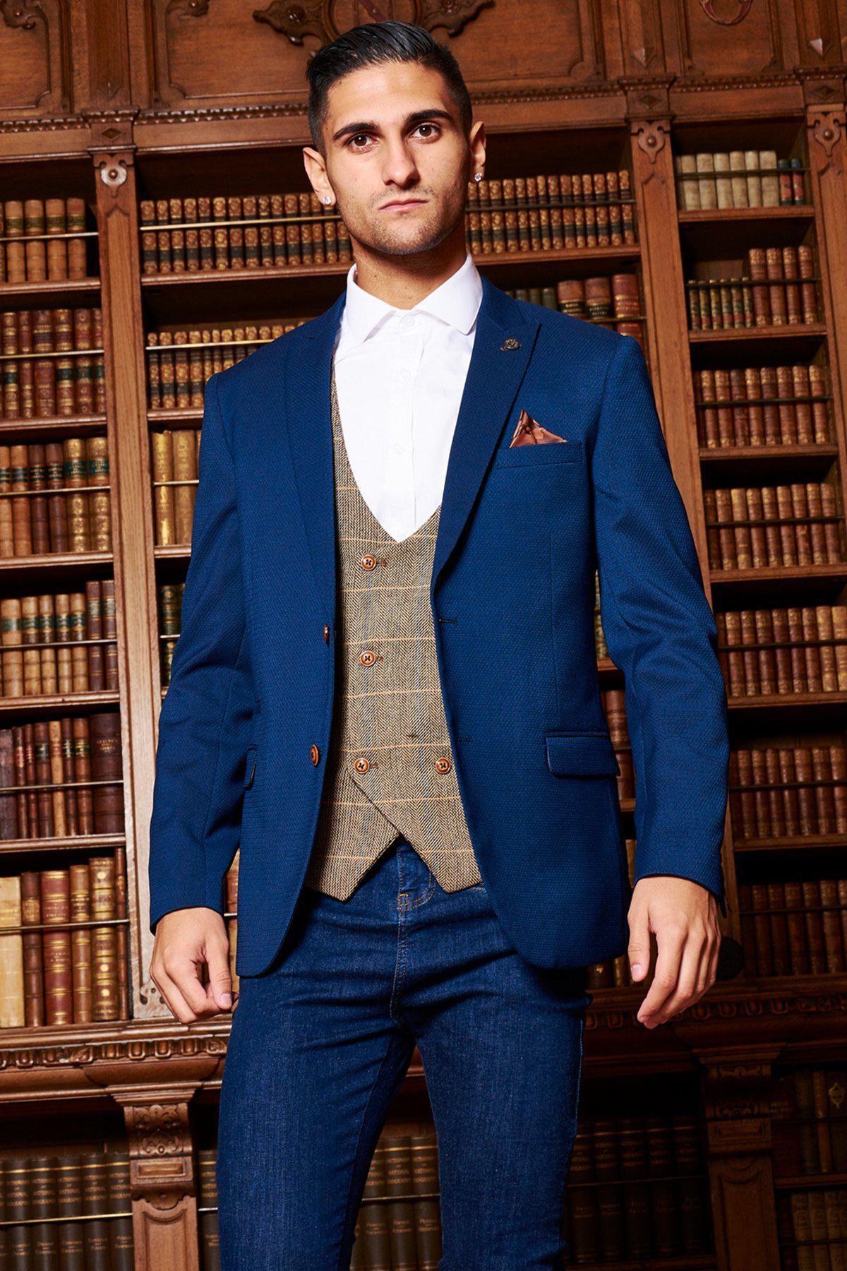 A man poses in front of bookshelves wearing the marcdarcy MAX Royal Blue Blazer with TED Waistcoat and jeans, highlighting a smart-casual style.