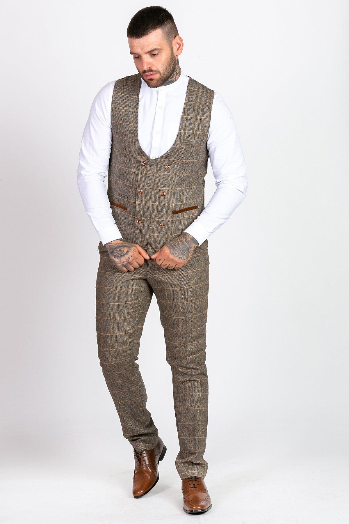 A man with tattoos wears the marcdarcy MAX - Royal Blue Blazer with TED Waistcoat over a white dress shirt and matching pants, paired with brown dress shoes. He stands against a plain white background, looking down with his hands clasped in front.