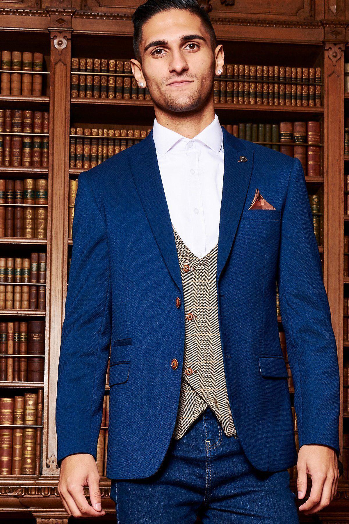 A man wearing the marcdarcy MAX Royal Blue Blazer with TED Waistcoat and a white shirt stands before library shelves, showcasing a smart-casual style.