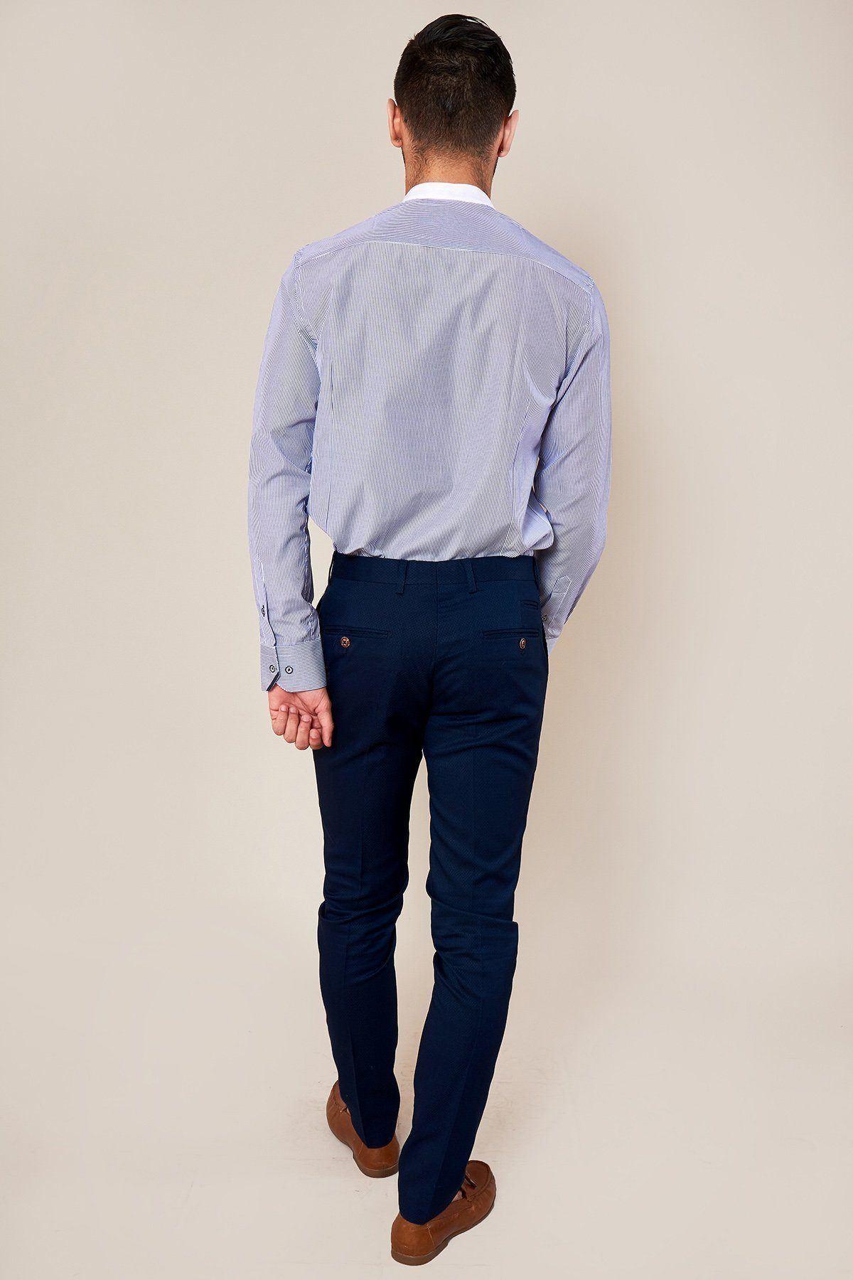 A man stands with his back to the camera, wearing a light blue dress shirt, marcdarcy’s MAX - Skinny Fit Navy Trousers, and brown loafers against a plain beige background.