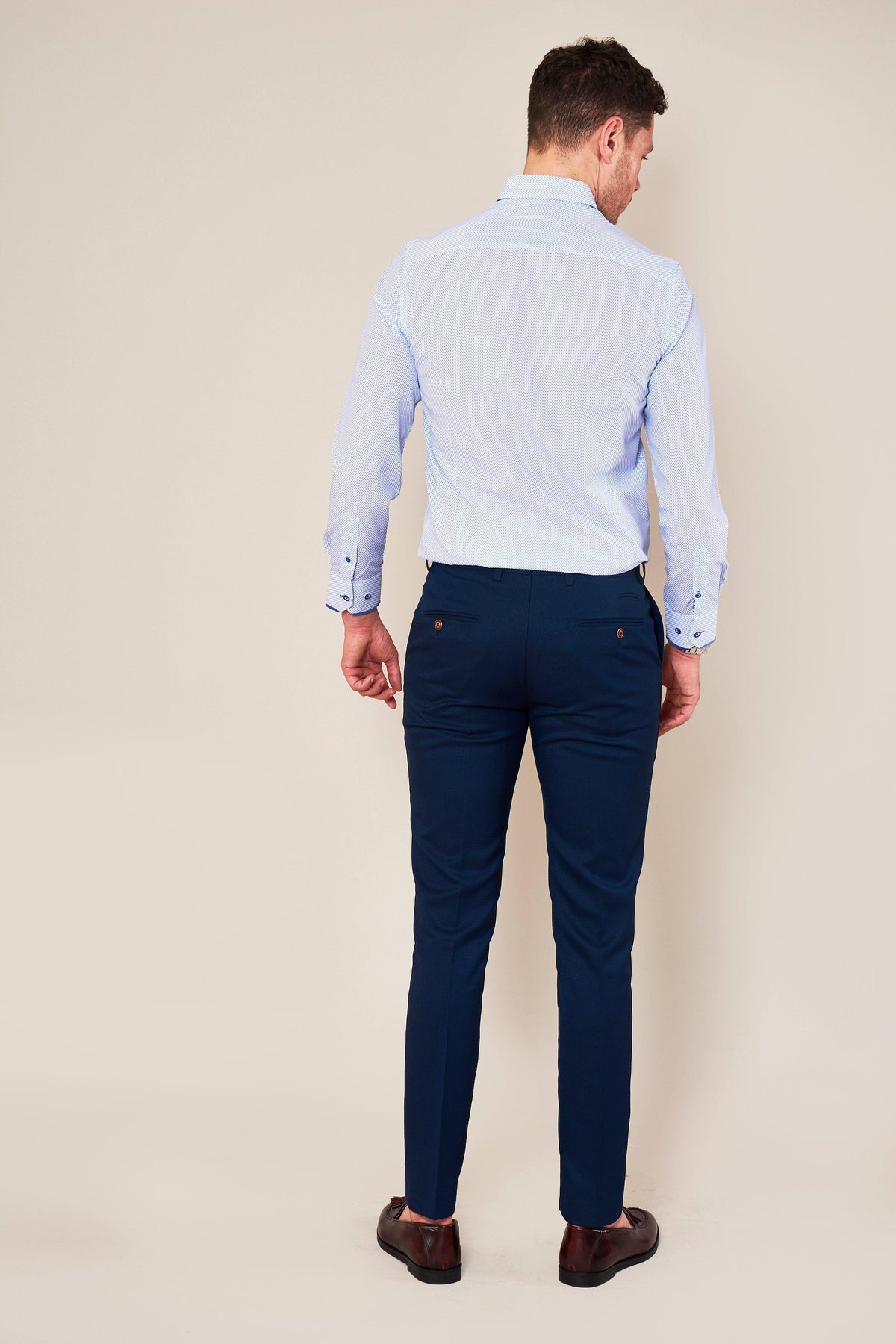 A man, seen from behind, wears a light blue dress shirt and marcdarcys MAX - Skinny Fit Royal Blue Trousers with brown dress shoes against a plain light background.