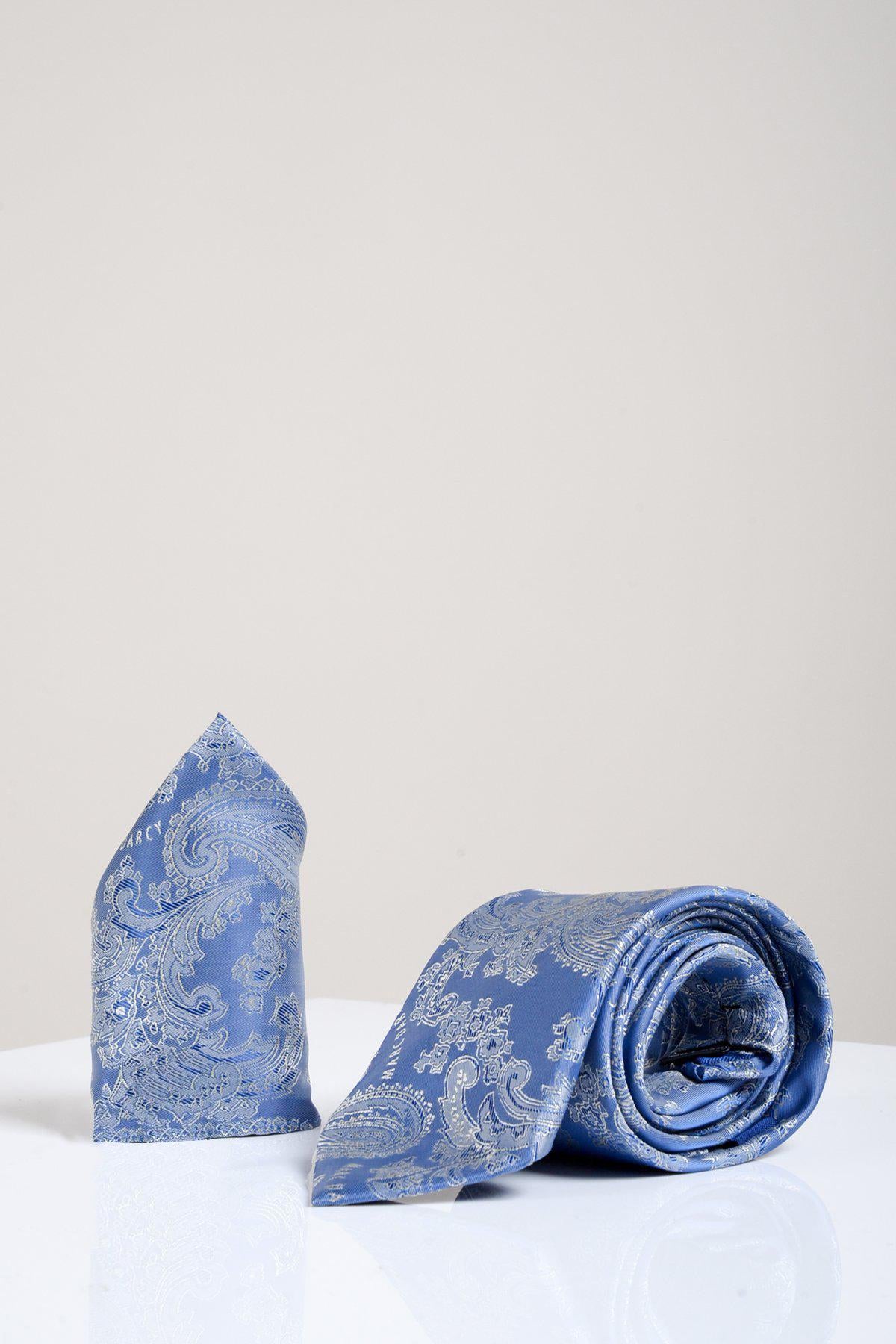 The Accessory MD PAISLEY Sky Blue Paisley Tie and Pocket Square Set, featuring a light blue paisley design, stands upright and rolled on a glossy white surface against a light gray background—ideal for refined formal looks.