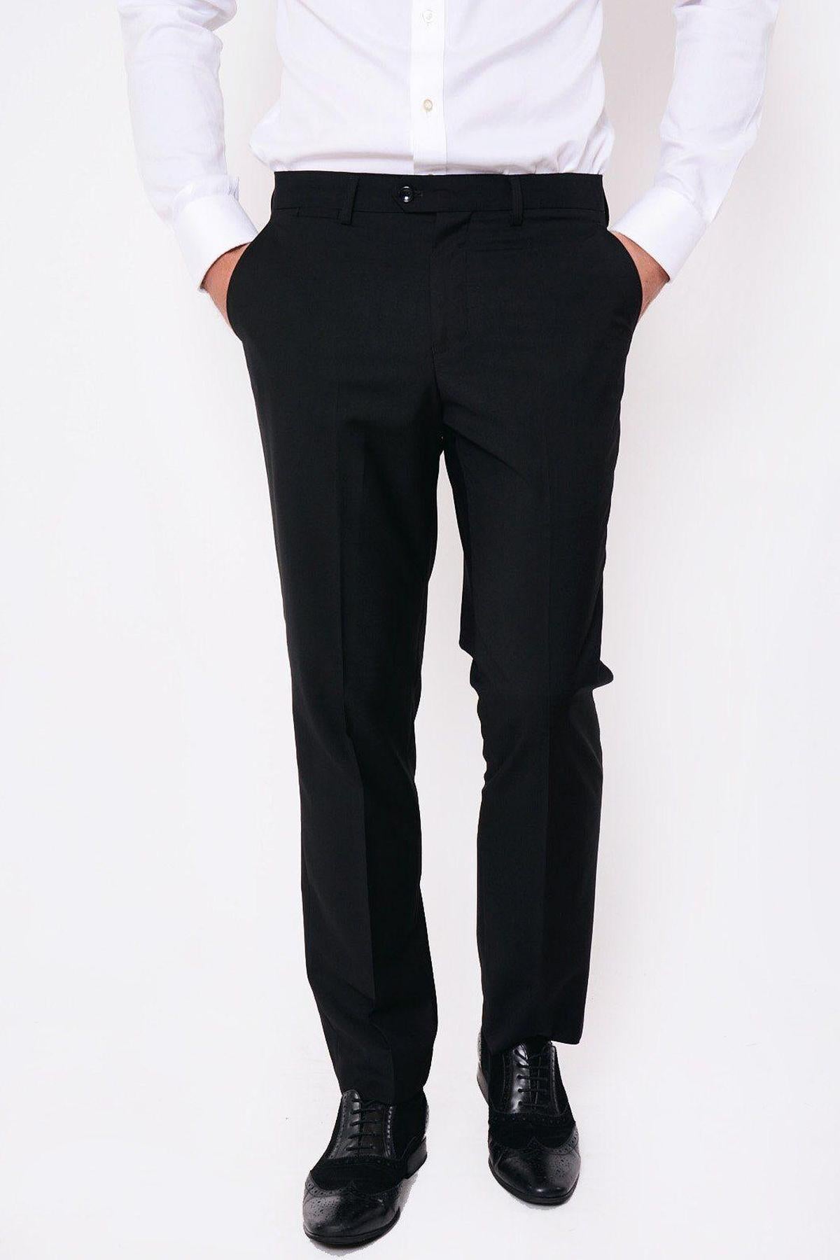 A man models marcdarcy’s RAMBO Black Flat Fronted Trousers with a white button-up shirt and black leather oxford shoes, hands in pockets against a white background—offering a modern spin on classic formal style.