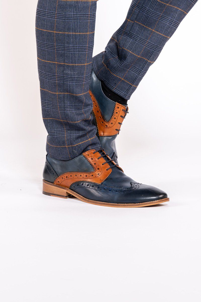 A person wearing Marc Darcys RILEY Navy Tan Leather Contrast Oxford Brogue Shoes with blue and brown plaid pants, standing on a white background.