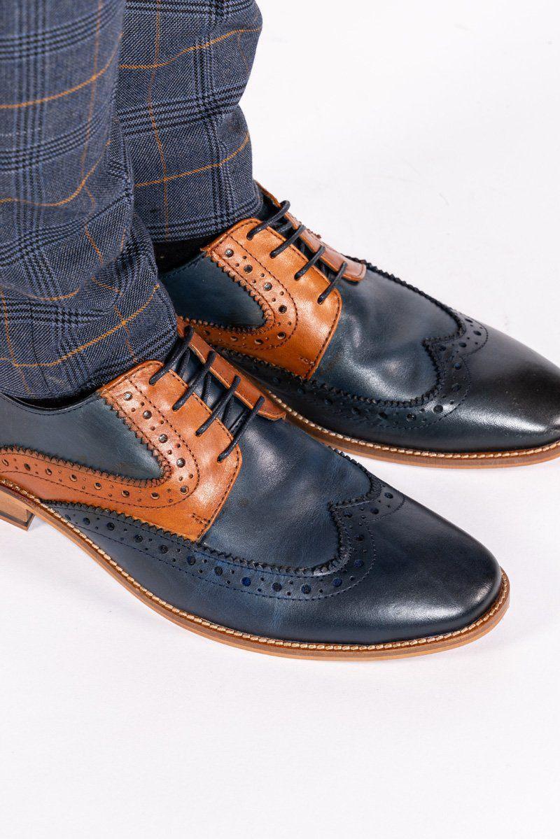 A person wearing Marc Darcys RILEY navy tan leather contrast Oxford brogue shoes with dark blue plaid pants stands on a white surface.