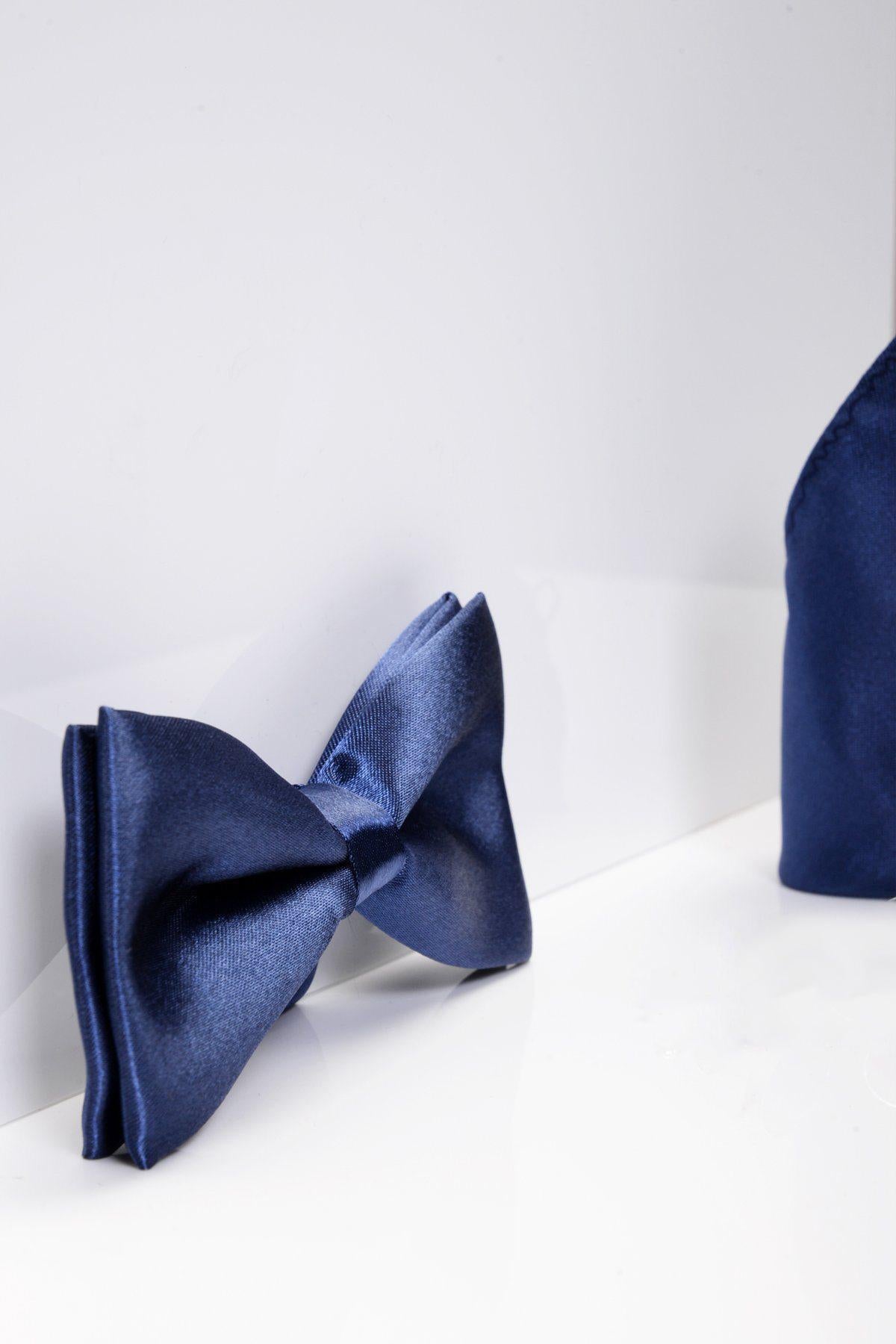 The STANLEY Satin Bow Tie and Pocket Square Set in Navy by Accessory rests on a white surface, with the pocket square partially visible to the right—an ideal choice for formal wear.