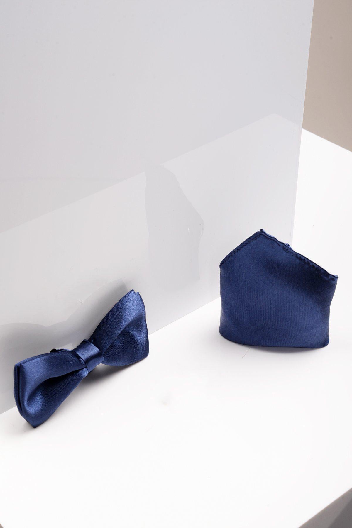The STANLEY Satin Bow Tie and Pocket Square Set in Navy by Accessory is shown on a white, reflective surface, ideal for formal wear.