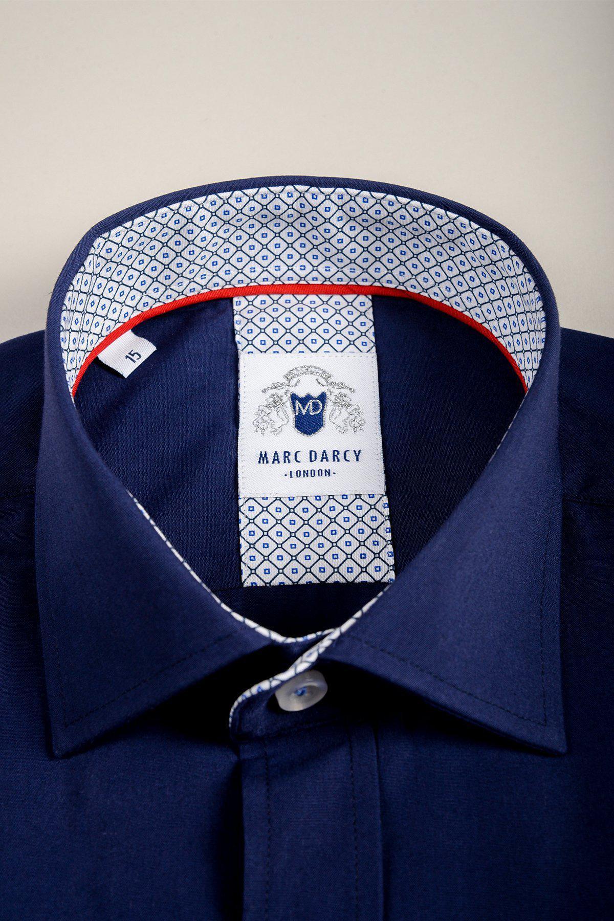A close-up of the marcdarcy SERGIO navy long sleeve shirt, made from a cotton blend with a patterned inner collar, red trim, and a white label featuring the brand name and logo.