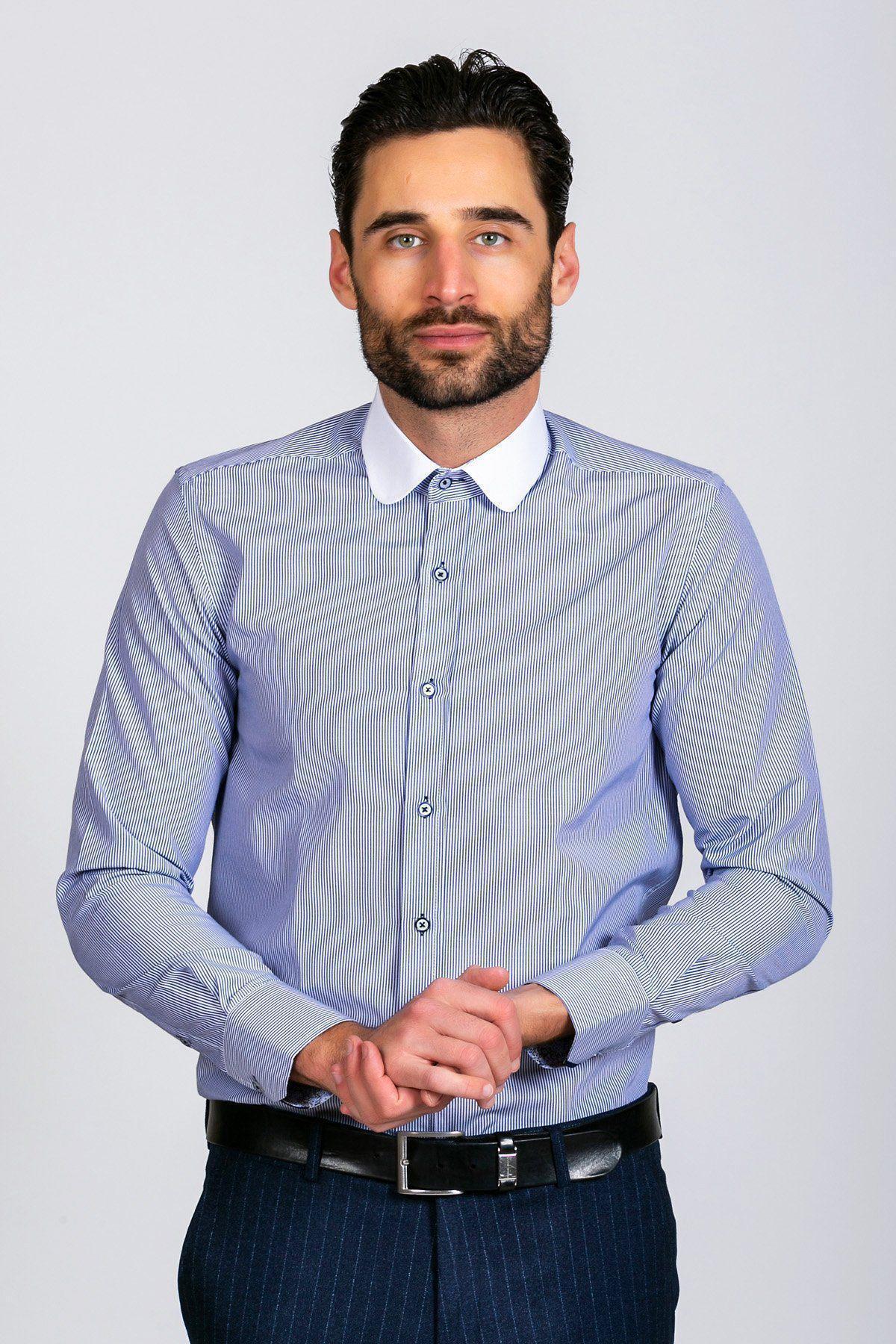 A style-conscious gent with dark hair and a beard wears the SHELBY Navy Blue Stripe Penny Collar Shirt by Marc Darcy, paired with dark trousers and a black belt, standing against a plain light background with hands clasped.
