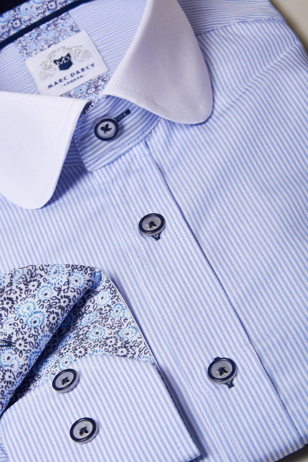 The SHELBY Sky Blue Stripe Penny Collar Shirt by Marc Darcy features blue and white pinstripes, a white collar, floral inner cuff detail, dark buttons, and a branded Marc Darcy label on the collar.